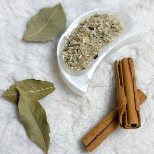 Spices including cinnamon sticks, bay leaves, and a spoonful of dried herbs on a white surface.