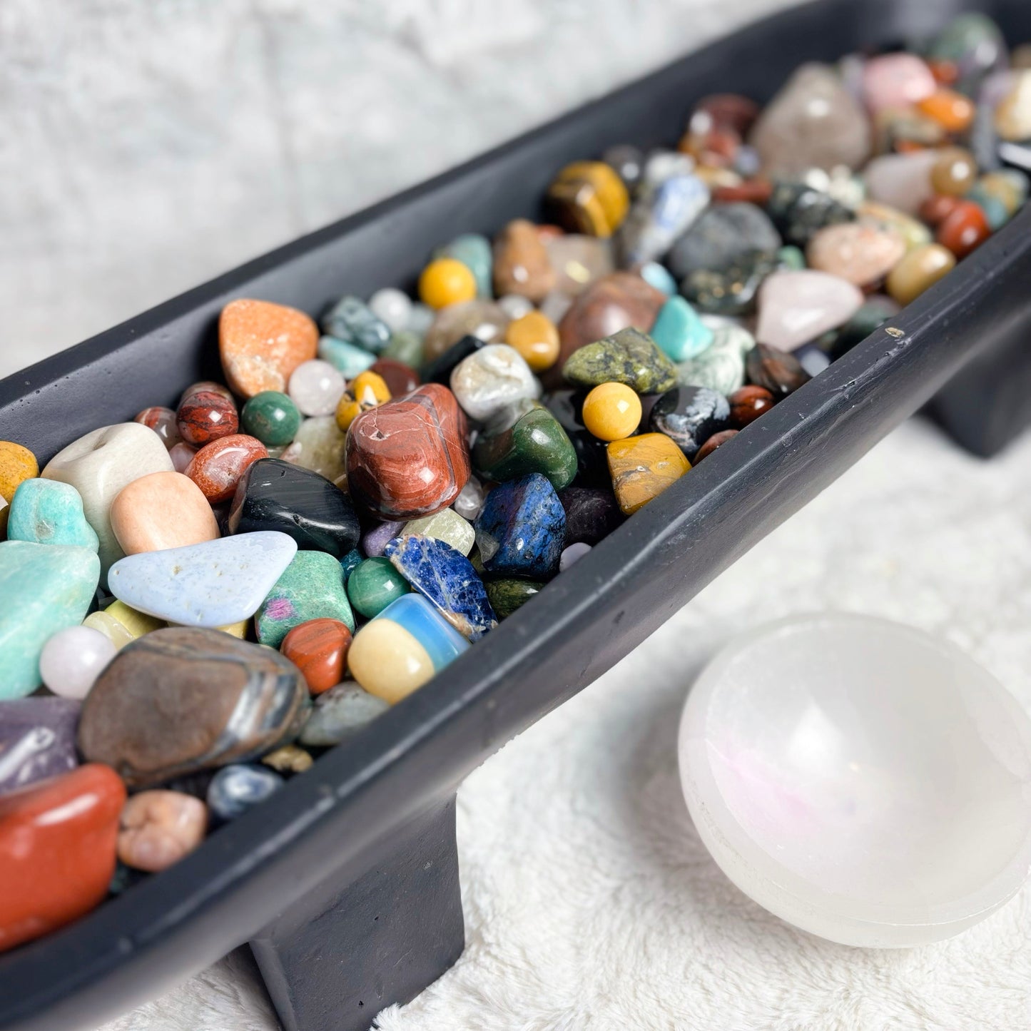 Assorted colorful stones in a black tray on a white surface