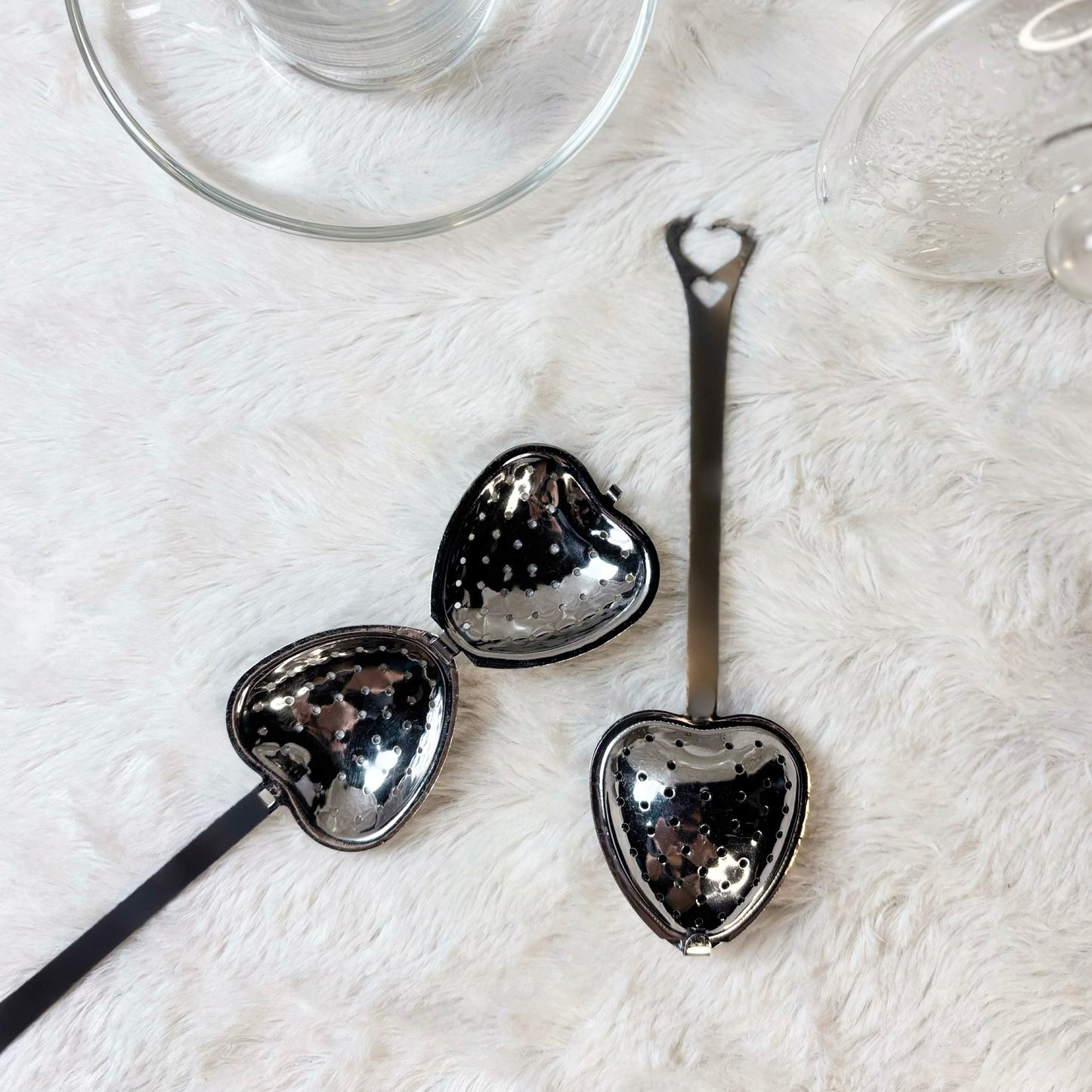 Heart-shaped metal spoons on a white surface with a clear glass in the background.