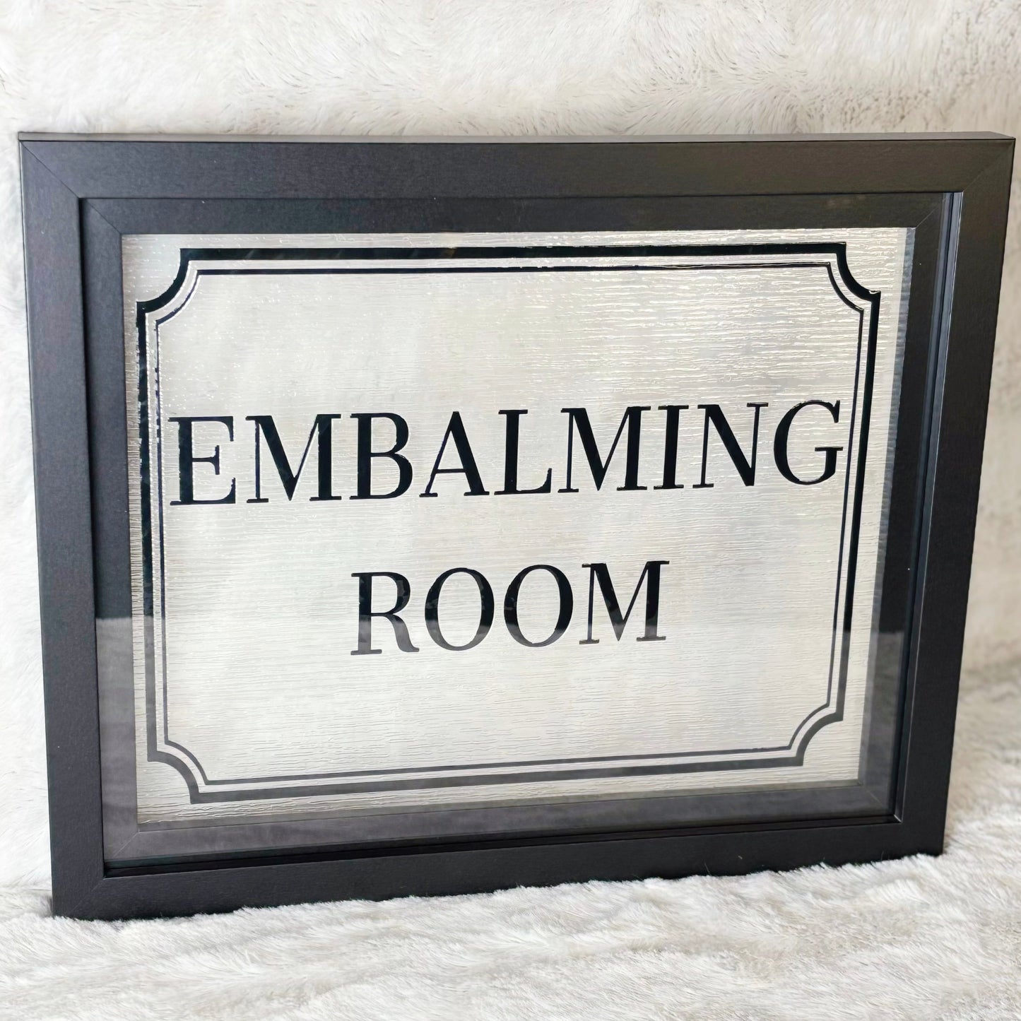 Framed sign with 'EMBALMING ROOM' text on a white background
