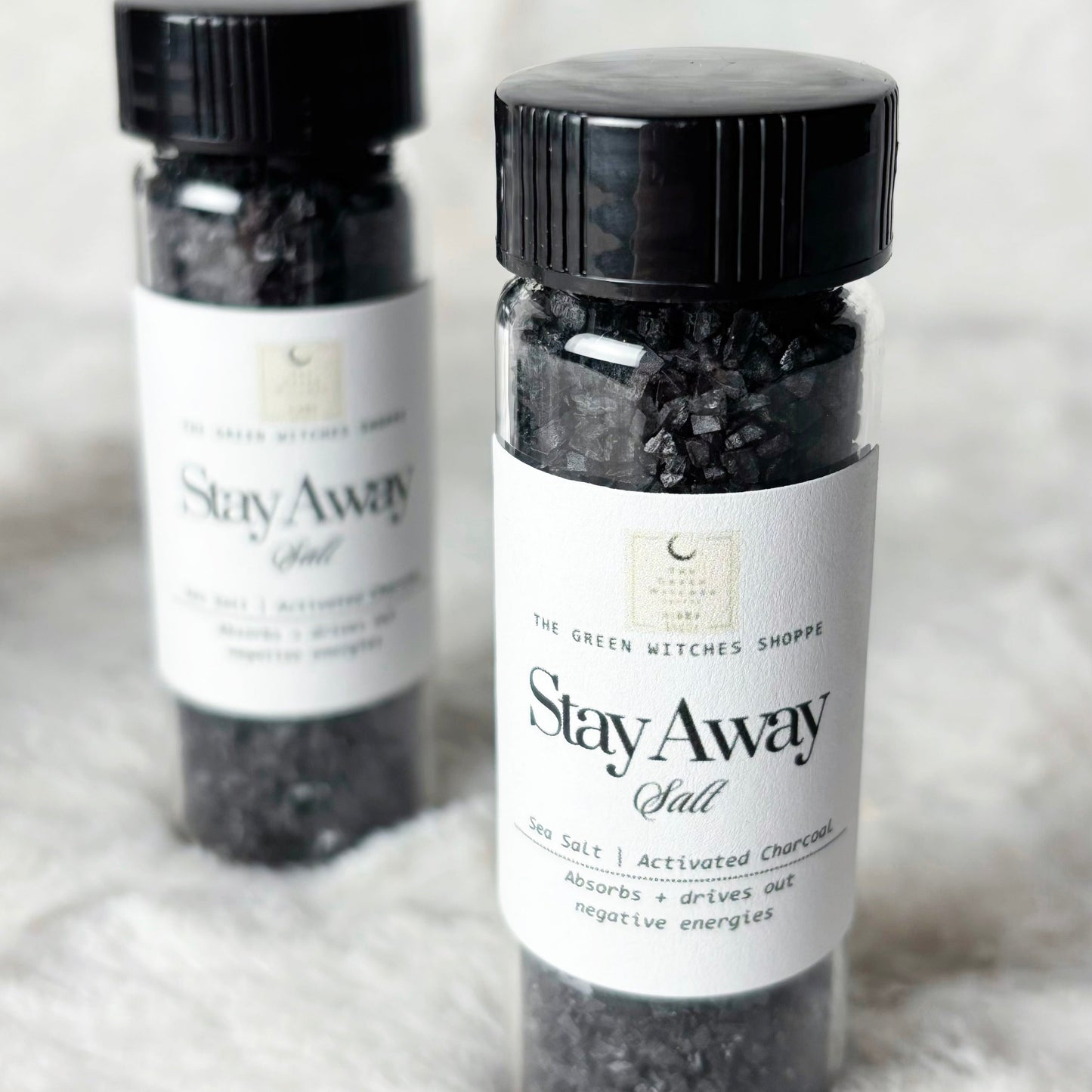 Two bottles of 'Stay Away Salt' with black lids on a light gray background