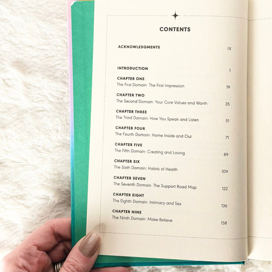 Open book with a hand holding it, displaying a table of contents on a soft white background.