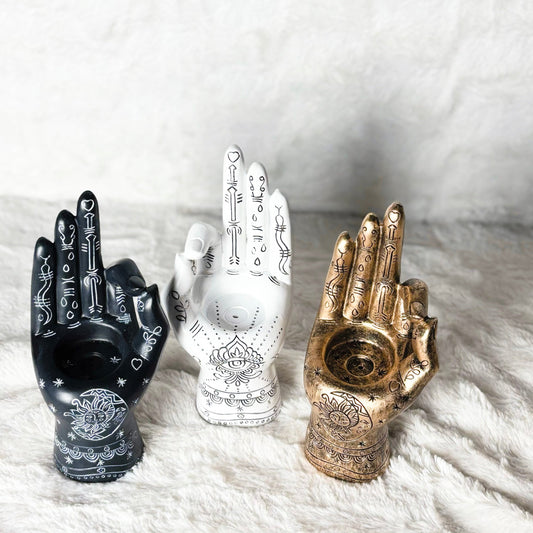 Three decorative hand-shaped objects in black, white, and gold on a textured white surface.