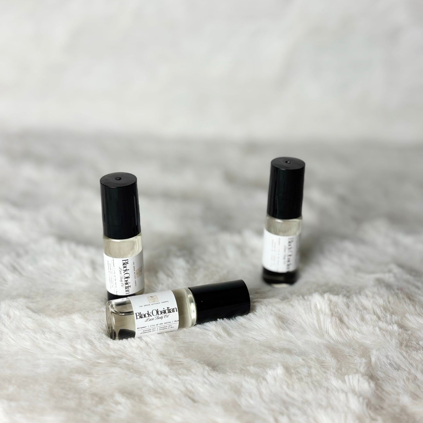 Three small perfume bottles with black caps on a white fur surface