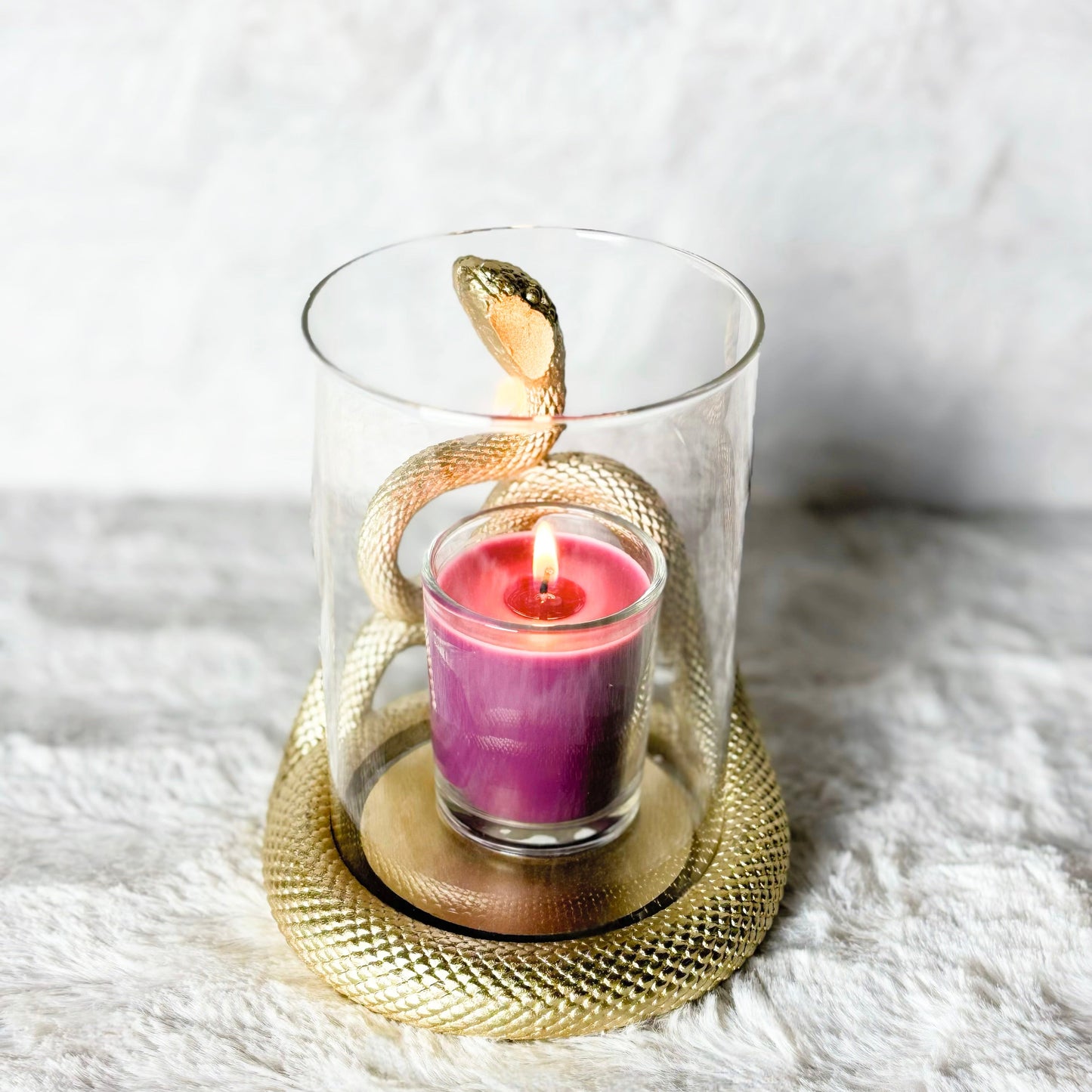 Decorative glass holder with a gold snake design around a purple candle on a white surface.