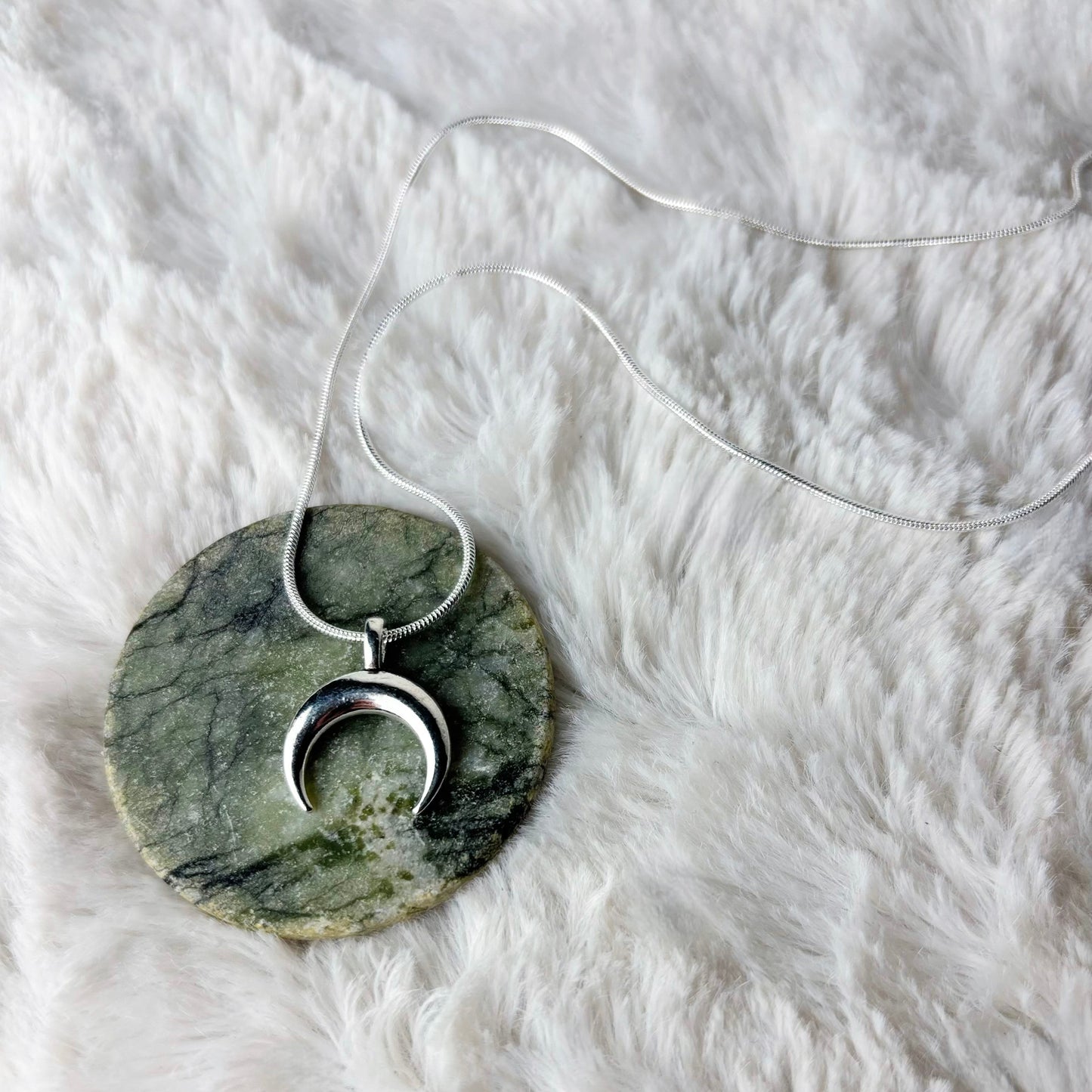 Marble-patterned pendant with silver crescent moon design on a white fur surface