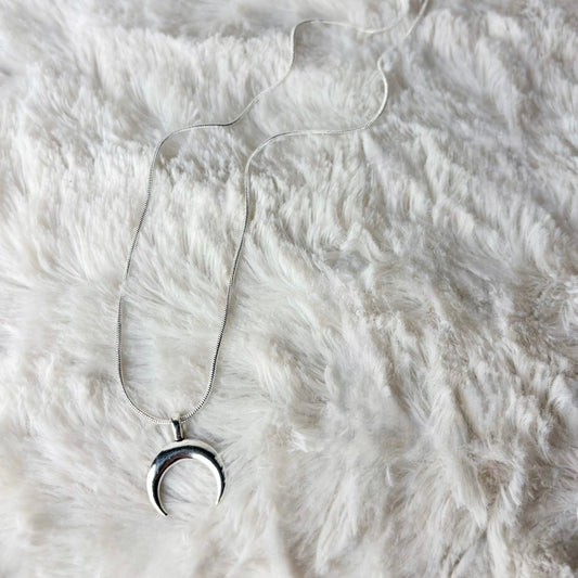 Silver necklace with a crescent moon pendant on a white fur surface