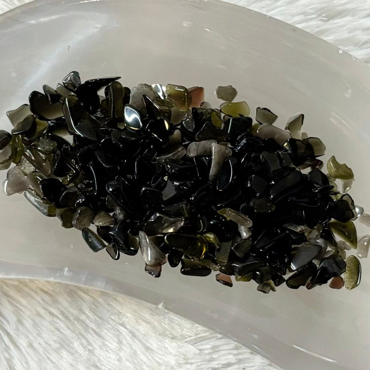 Crystal dish with crystals on a white fur surface surrounded by small bottles.