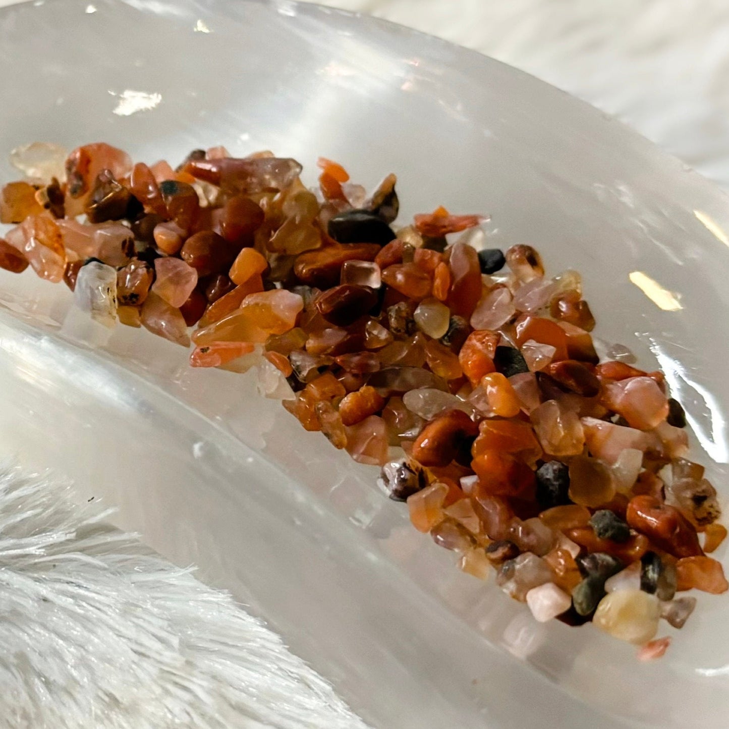 Crystal grid with orange crystals on a white surface next to a small jar labeled 'Carnelian'.