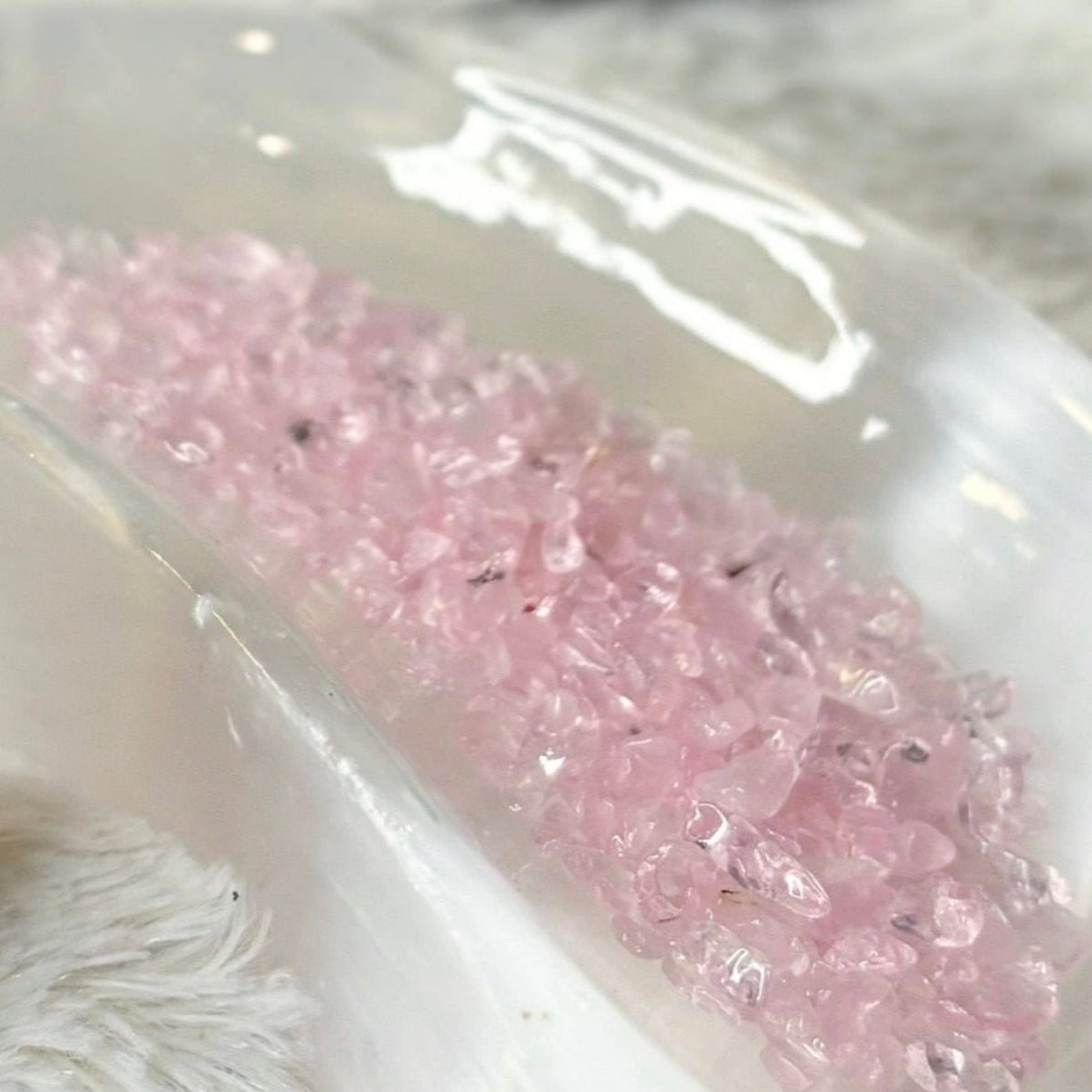 Rose Quartz crystal in a small bottle with pink crystals on a white dish, on a fluffy white surface.