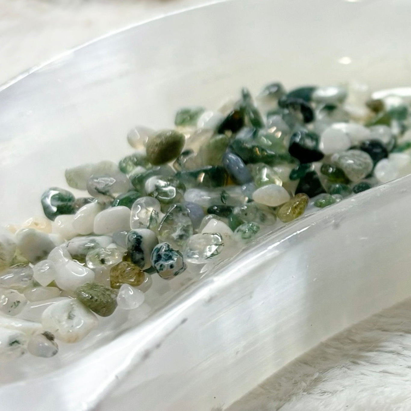 Moss Agate stones in a white dish with a bottle labeled 'Moss Agate' on a white fur background.