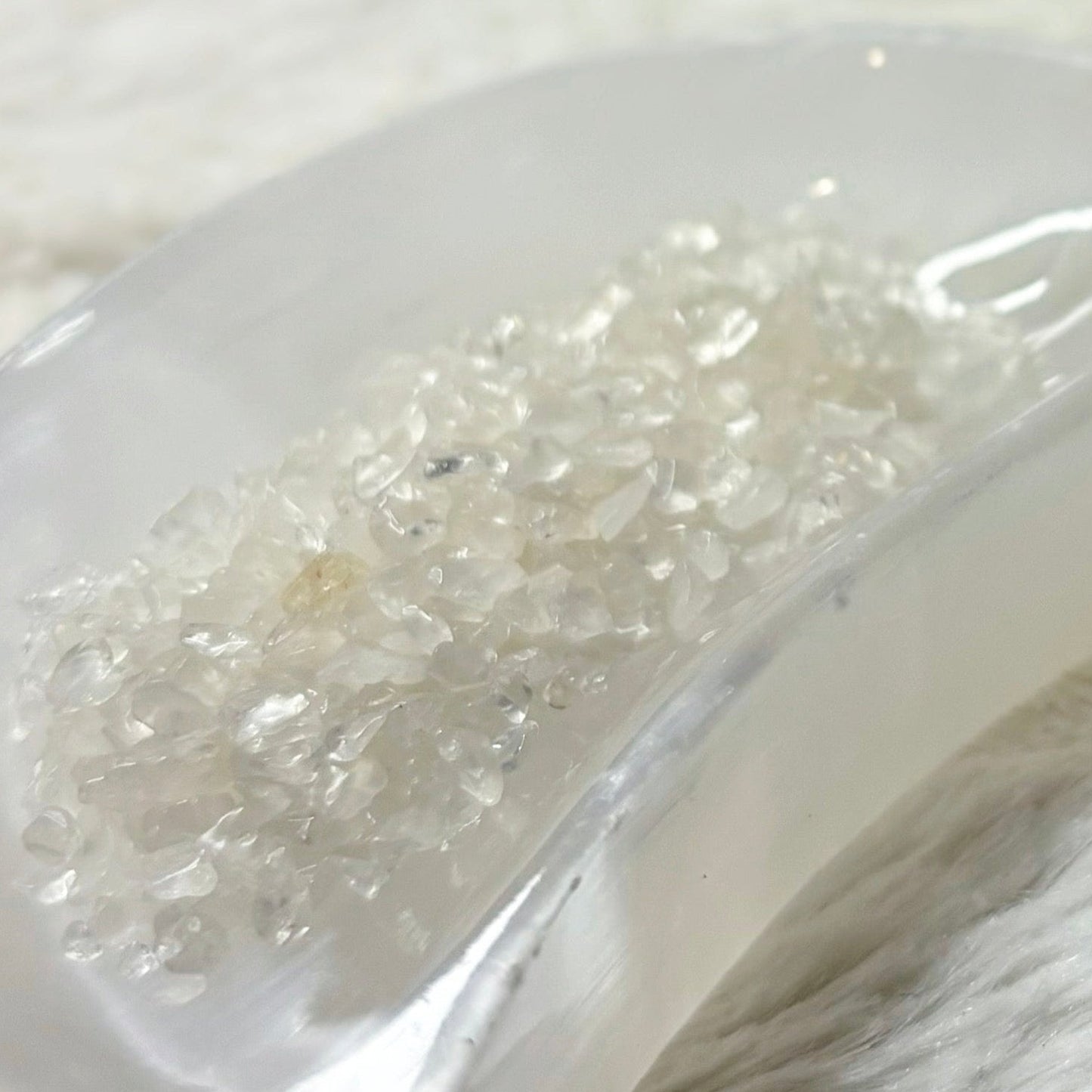 Clear crystal bottle labeled 'Clear Quartz' next to a white crystal dish on a textured surface.