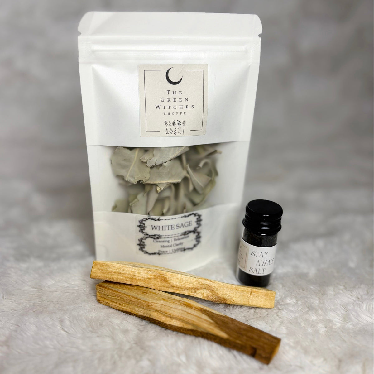 White bag labeled 'White Sage' with two wooden sticks and a small bottle on a gray background