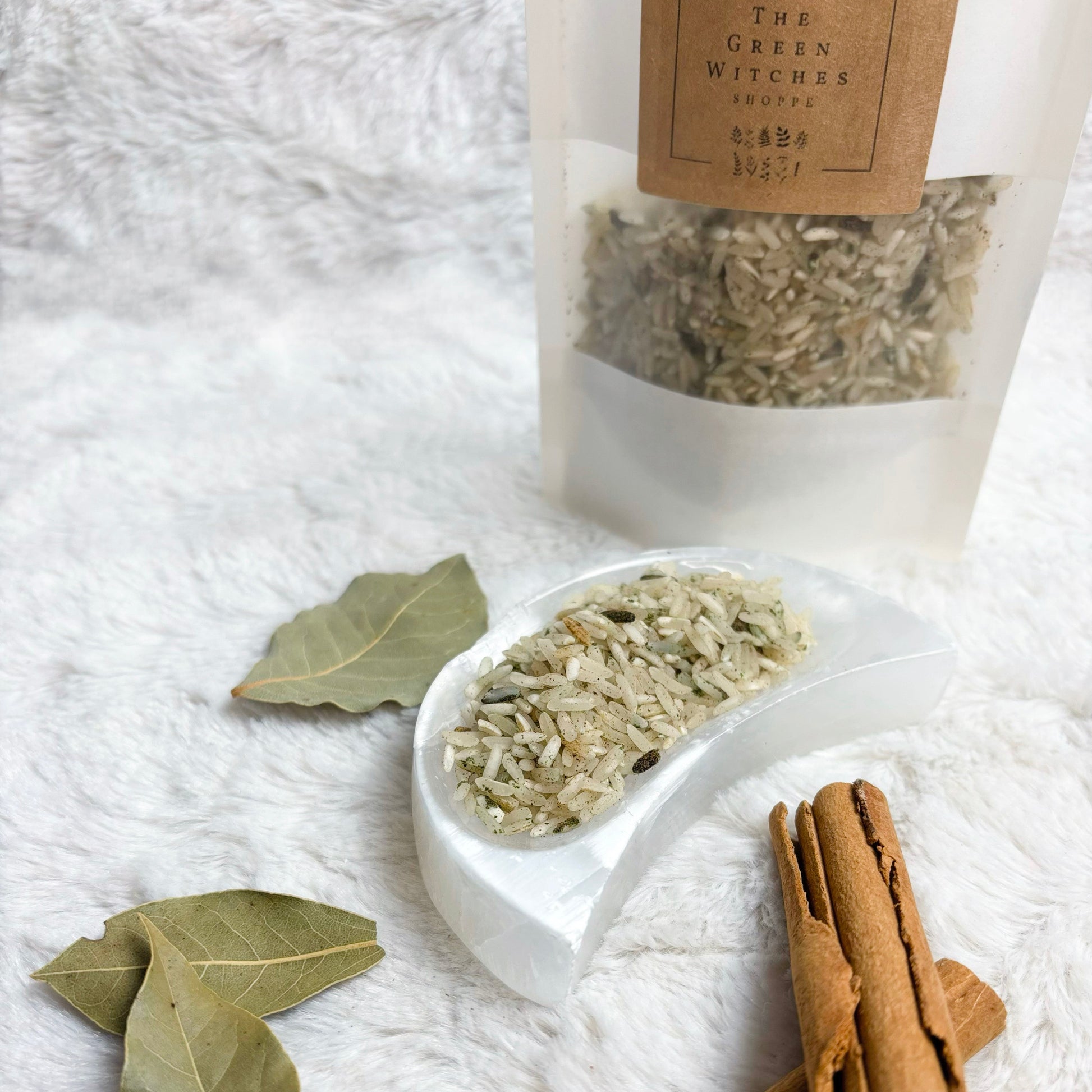 Herbal ingredients including cinnamon sticks and leaves on a white textured surface with a package labeled 'The Green Witches' in the background.