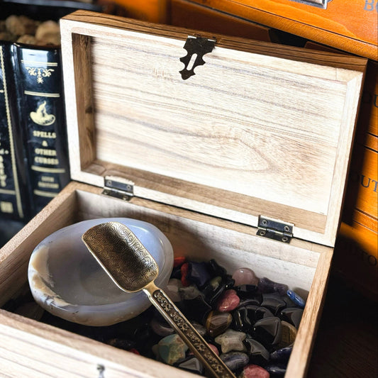 Wooden box with a spoon and stones inside, on a dark surface with books in the background.