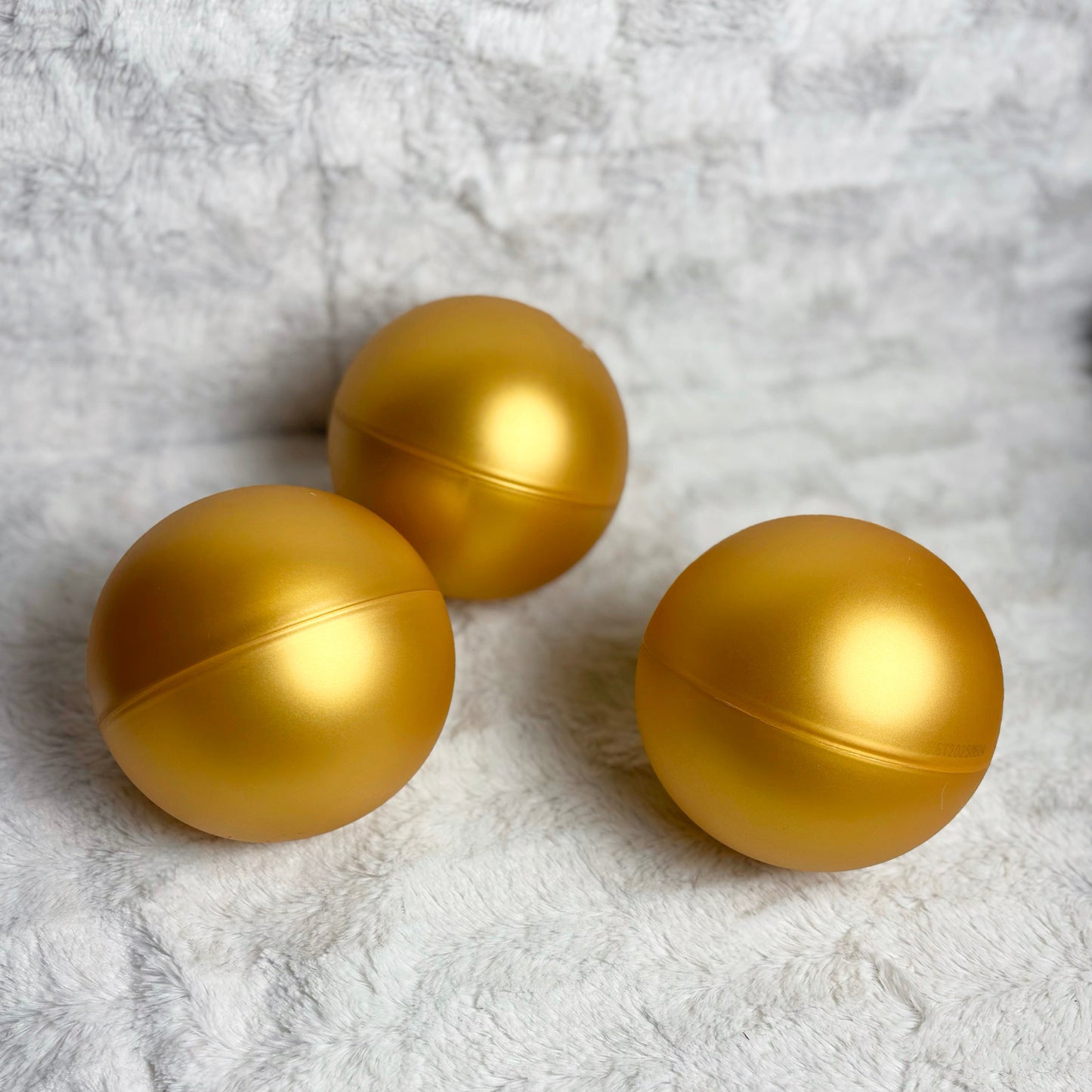 Three gold spherical objects on a textured white surface