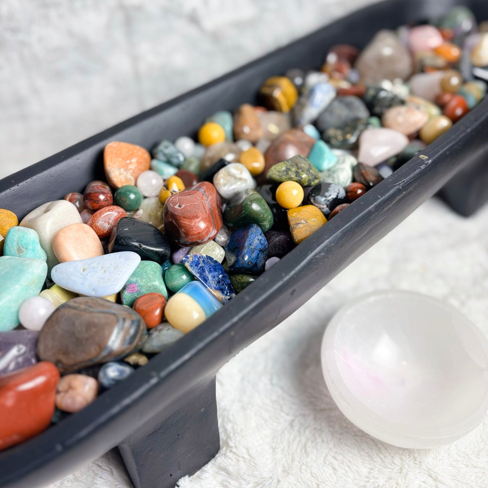 Assorted colorful stones in a black tray on a white surface