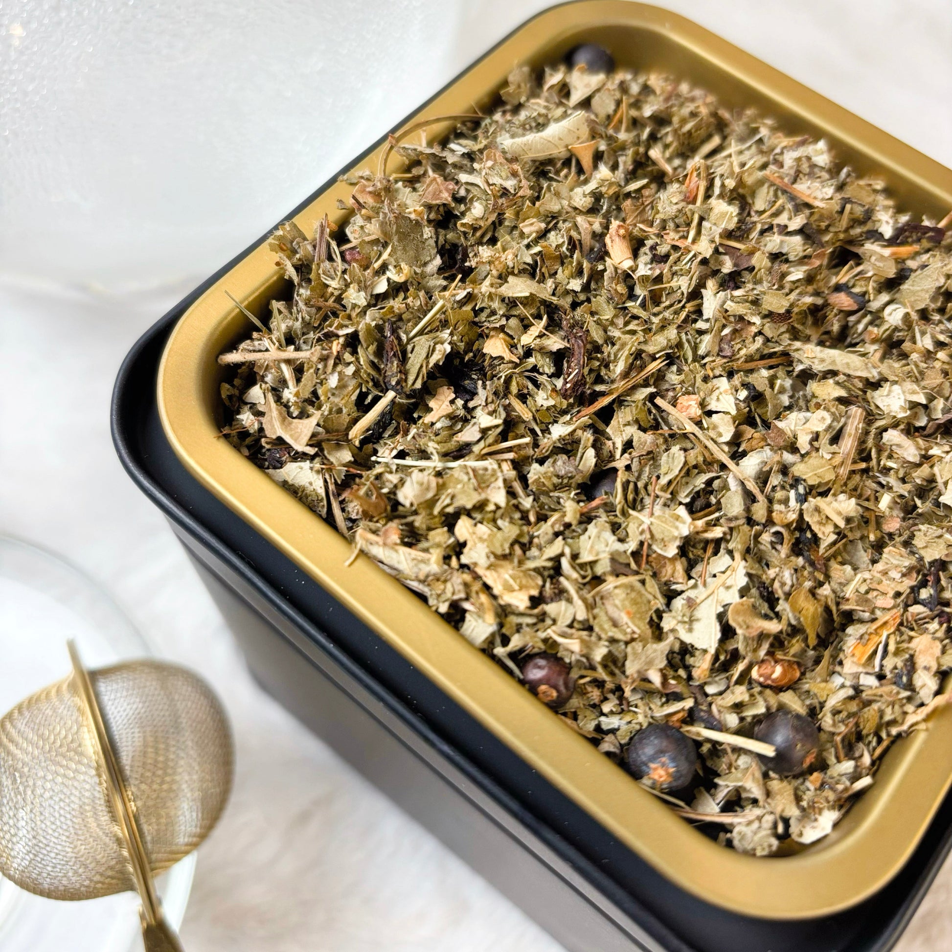Herbal tea leaves in a black and gold tin on a white background