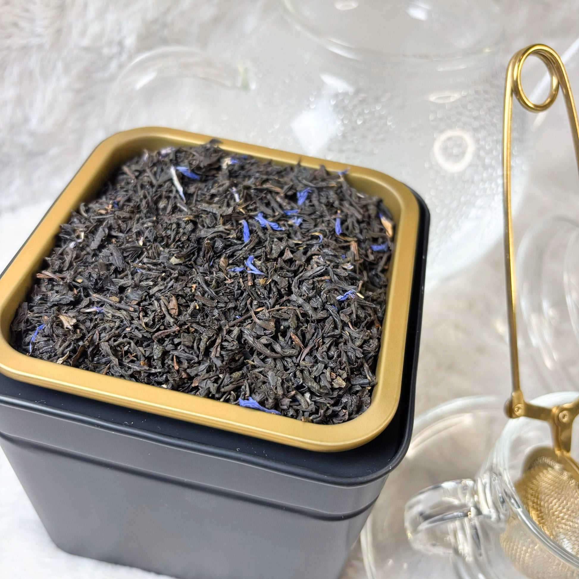 Square black tin filled with dried lavender flowers on a white background