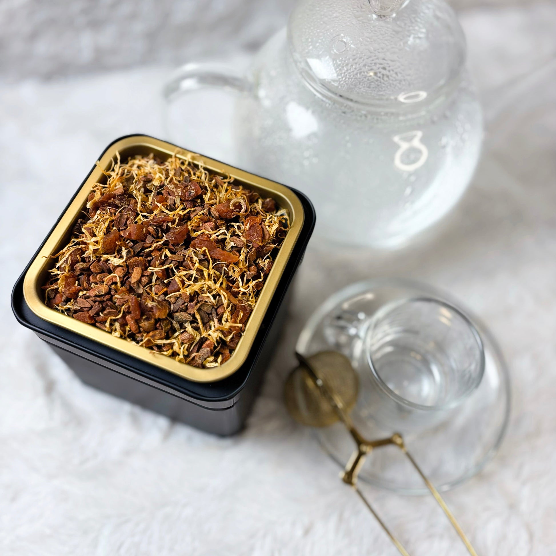 Square black container with dried herbs on a white fabric background