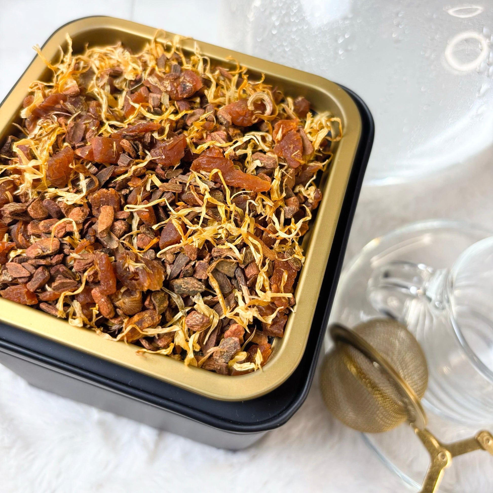 Herbal tea leaves in a black container with a clear lid on a white background