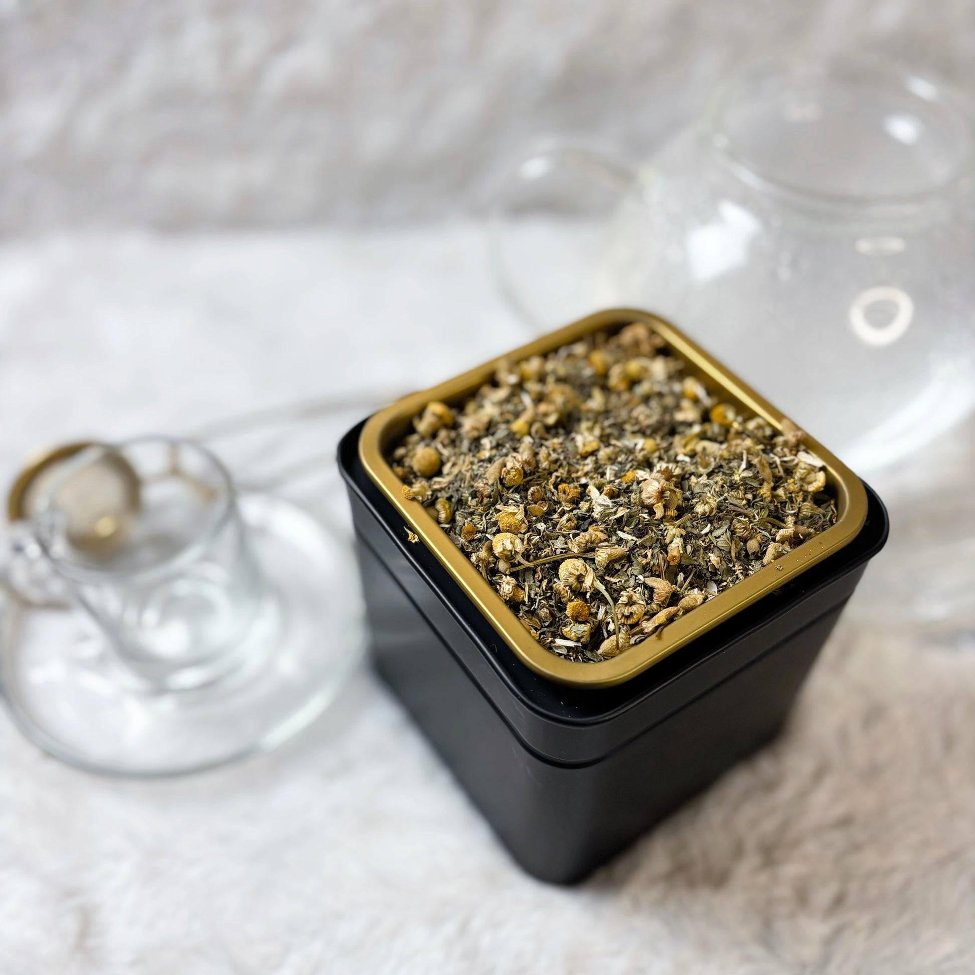 Black container with gold lid filled with a green substance on a white textured surface.
