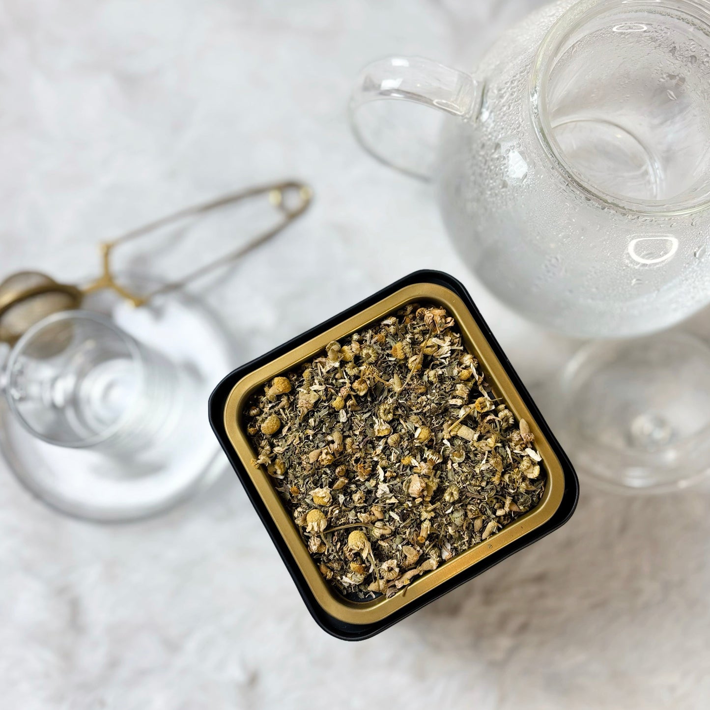 Tea infuser with gold accents on a white surface next to a teapot