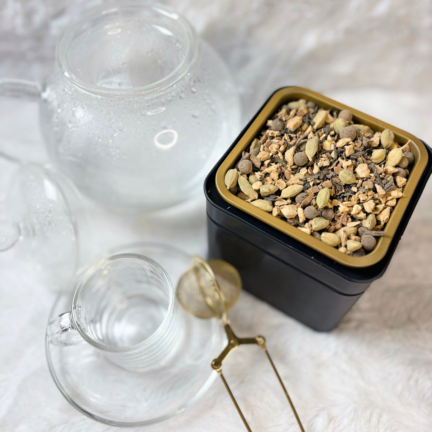 Clear glass teapot and cup with a container of loose tea leaves on a white textured surface