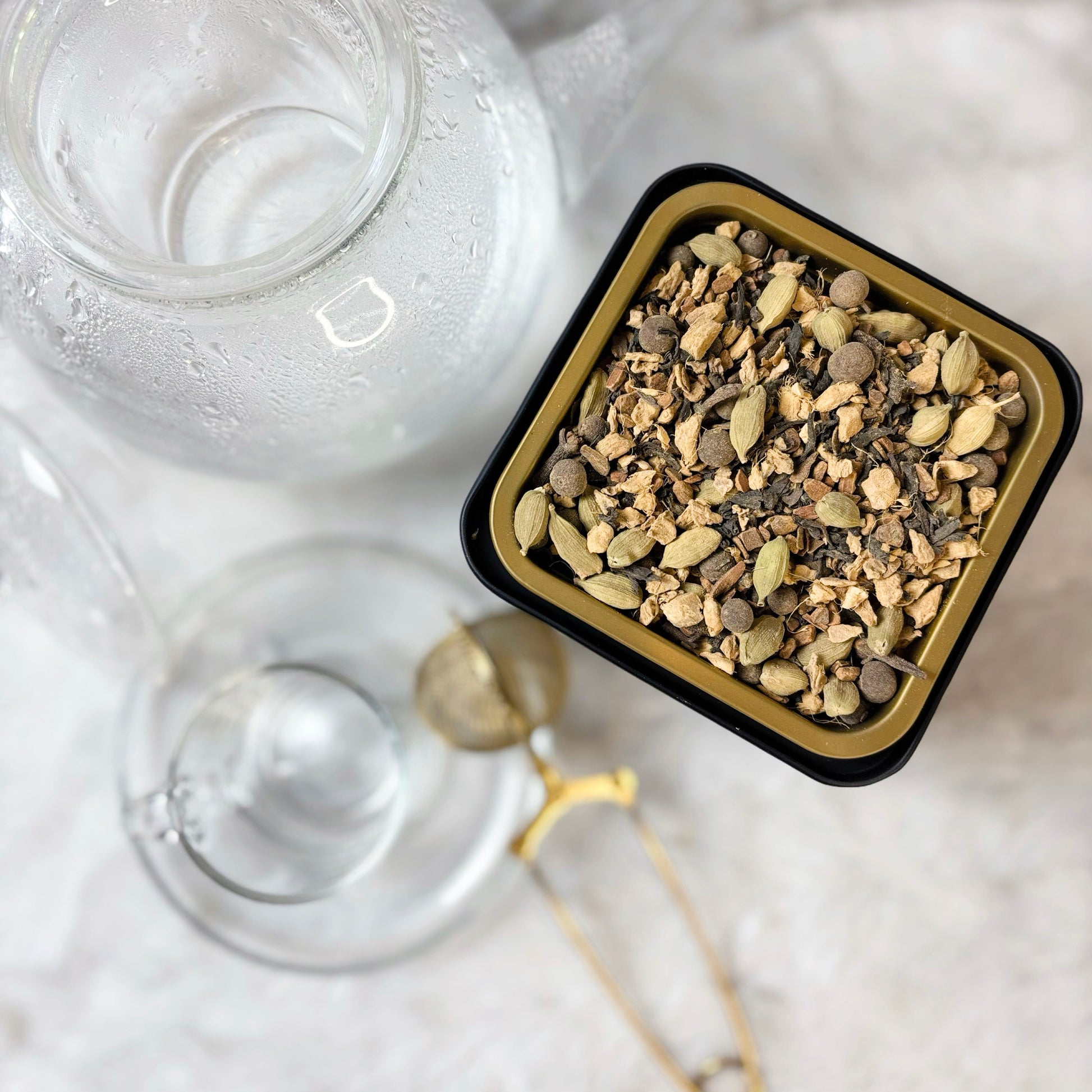 Clear glass container with lid and a small black container of herbs on a marble surface