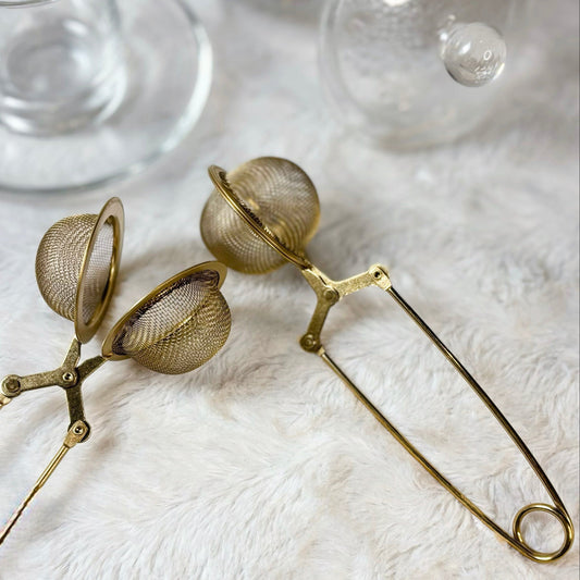 Decorative tea infuser with spherical mesh ends on a white surface