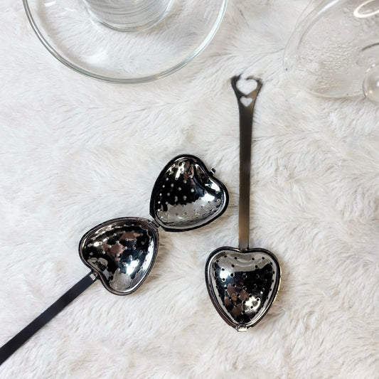 Heart-shaped metal spoons on a white surface with a clear glass in the background.