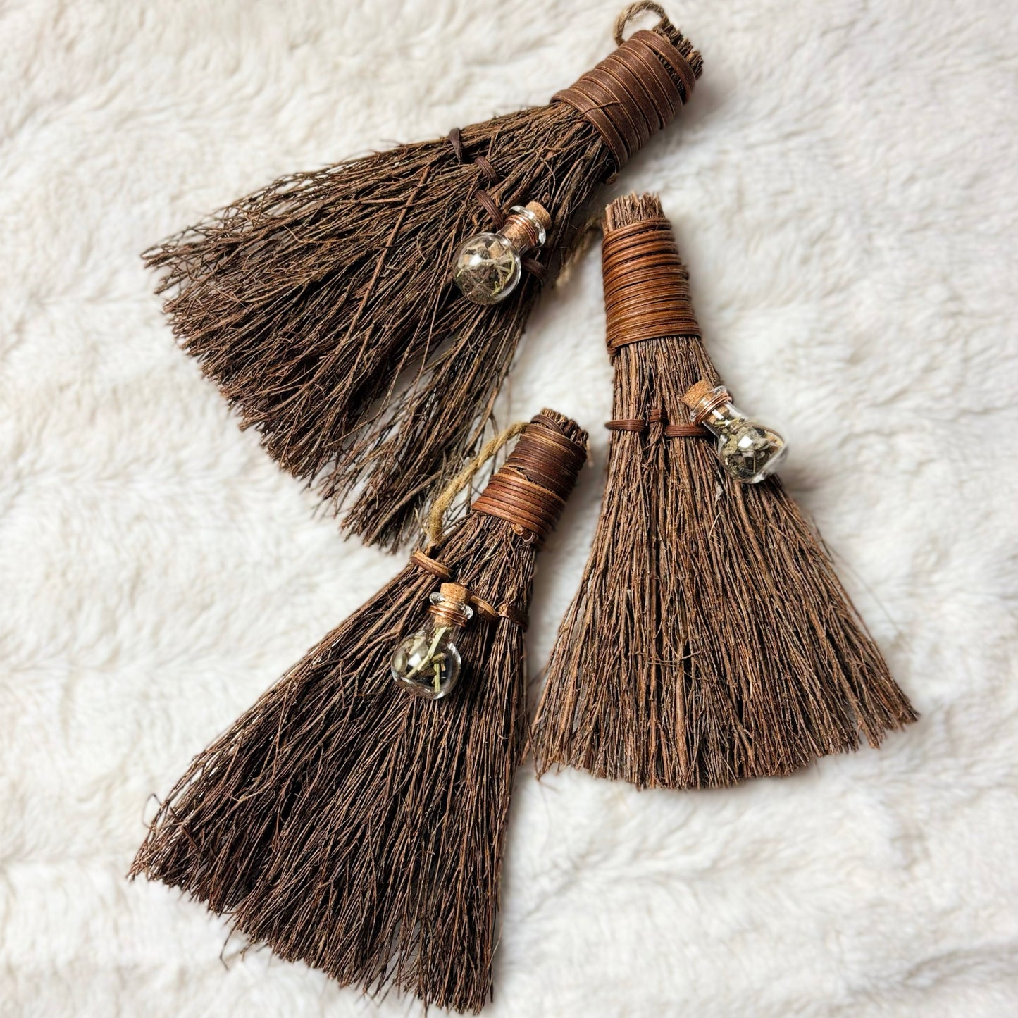 Three brown broom ornaments with decorative elements on a textured white surface
