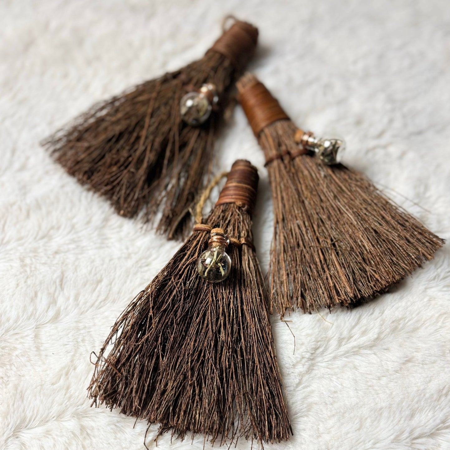 Three brown broom-like objects with tassels on a textured white surface