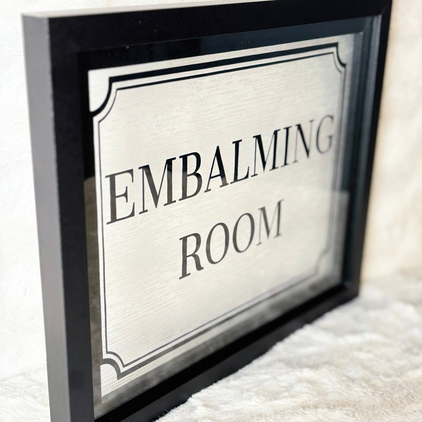 Framed sign with 'EMBALMING ROOM' text on a white background