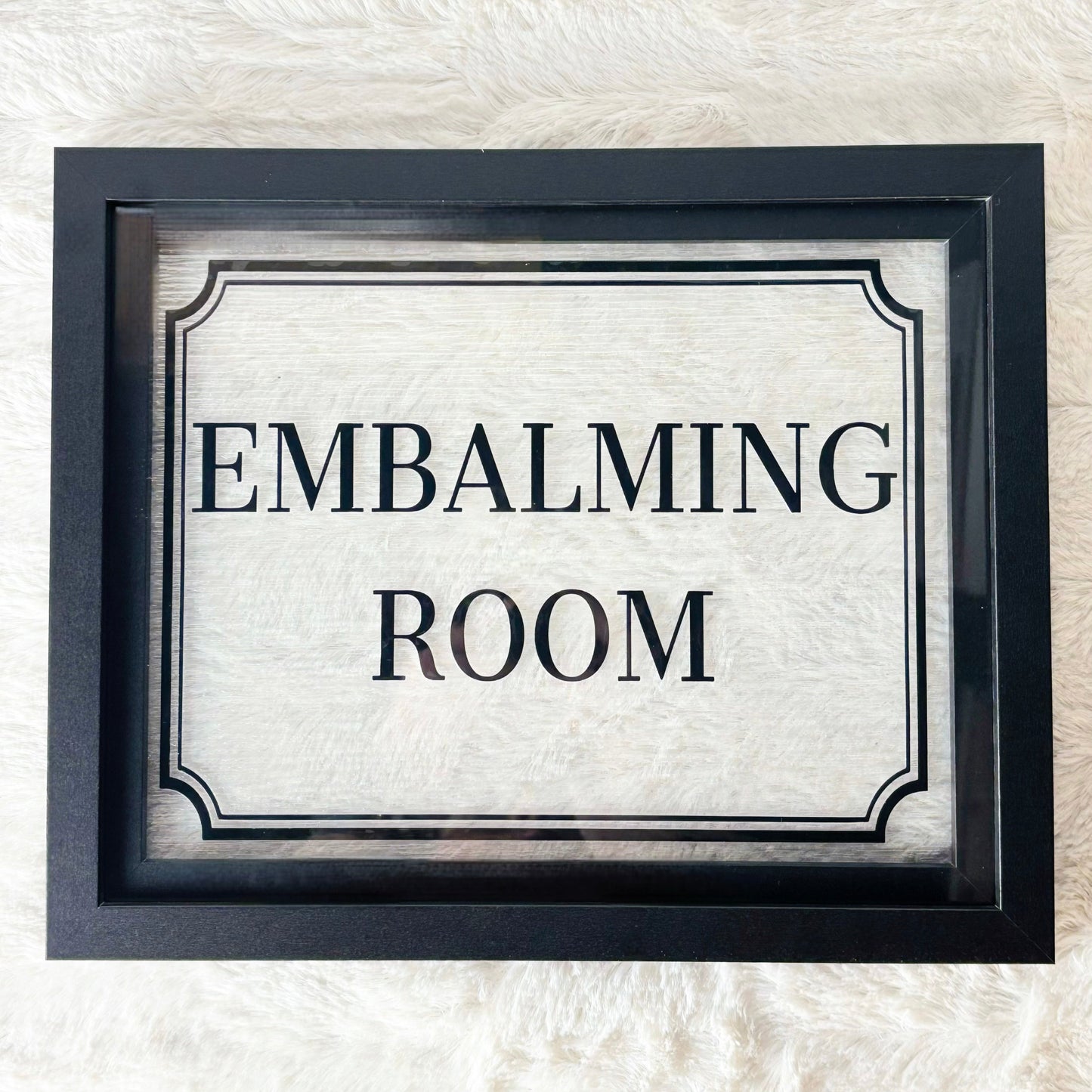 Framed sign with 'EMBALMING ROOM' text on a textured white background