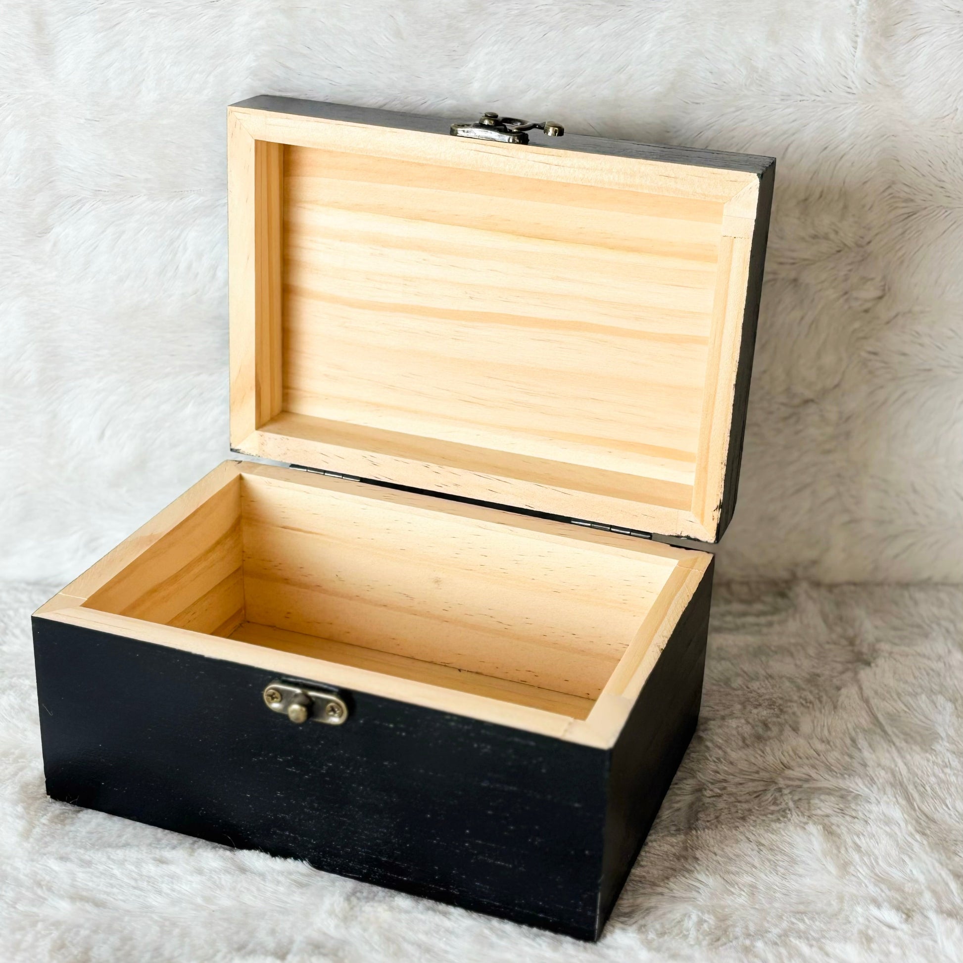 Black wooden box with a light wood interior on a textured white background