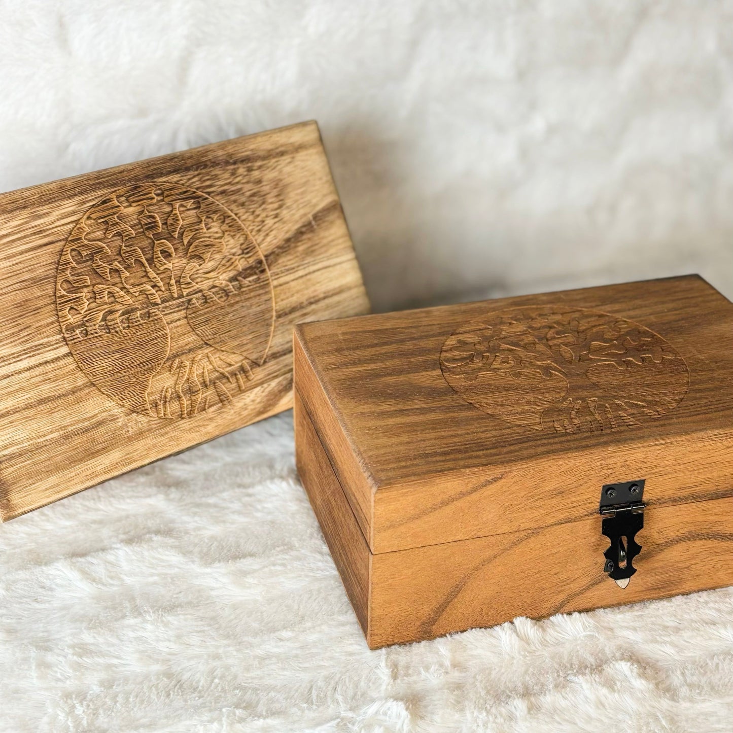 Two wooden boxes with engraved designs on a textured white surface