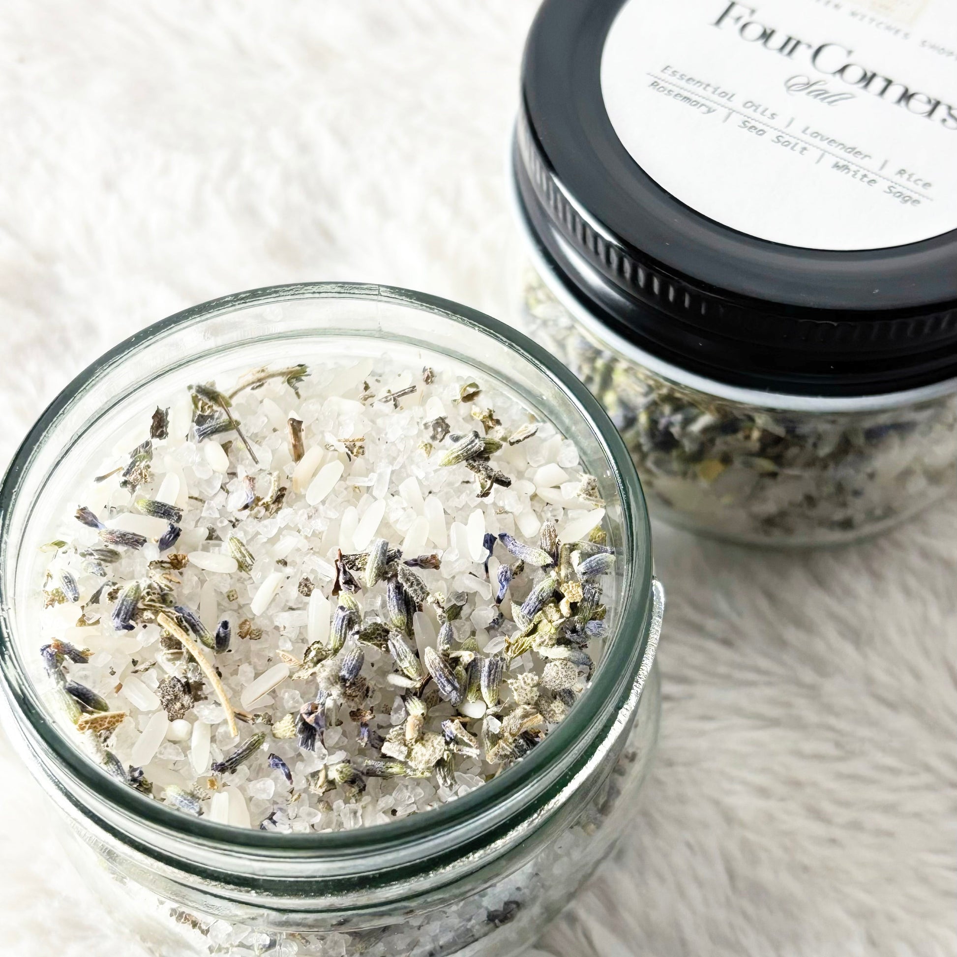 Two glass jars with bath salts and a label on a textured white surface