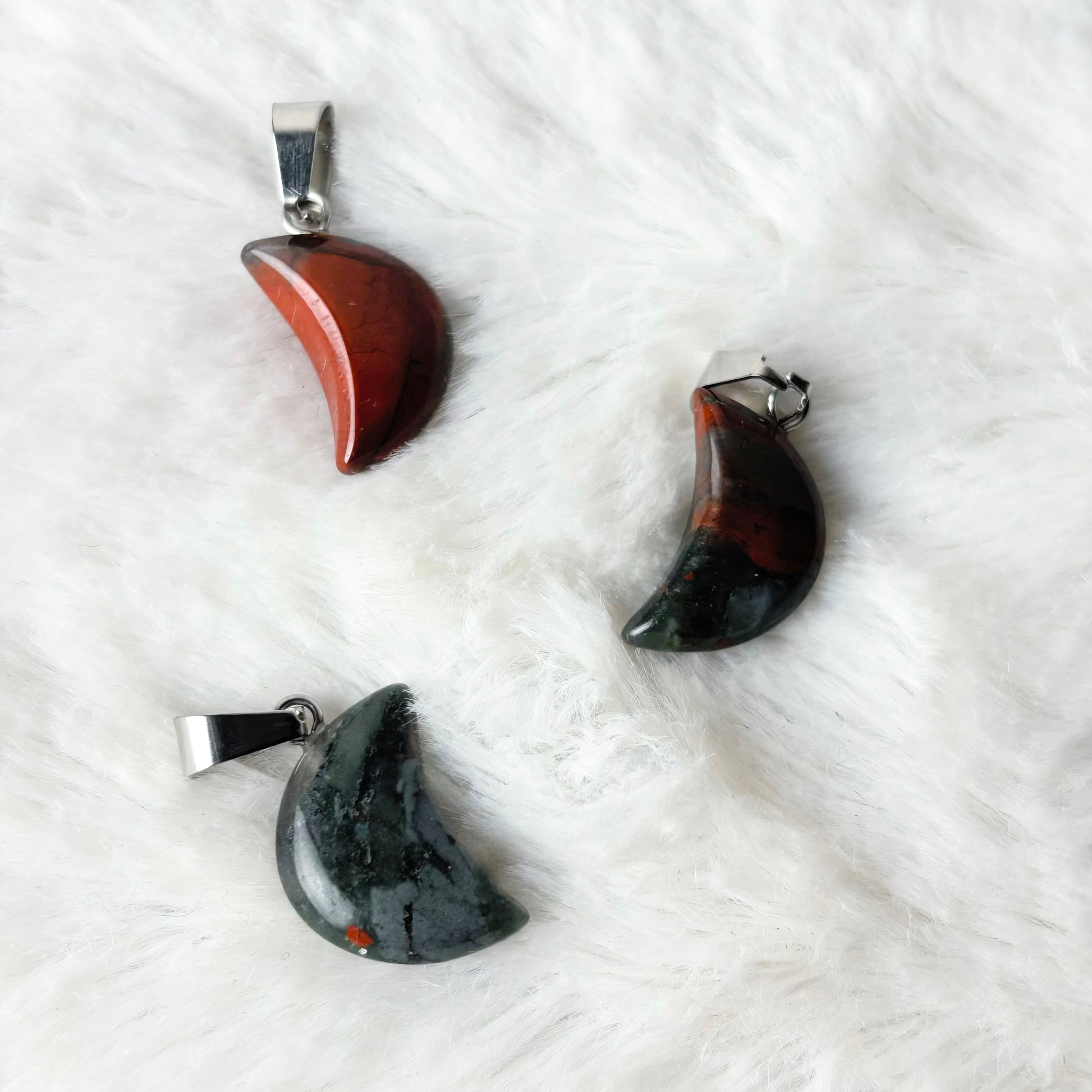Three moon-shaped pendants on a white textured surface