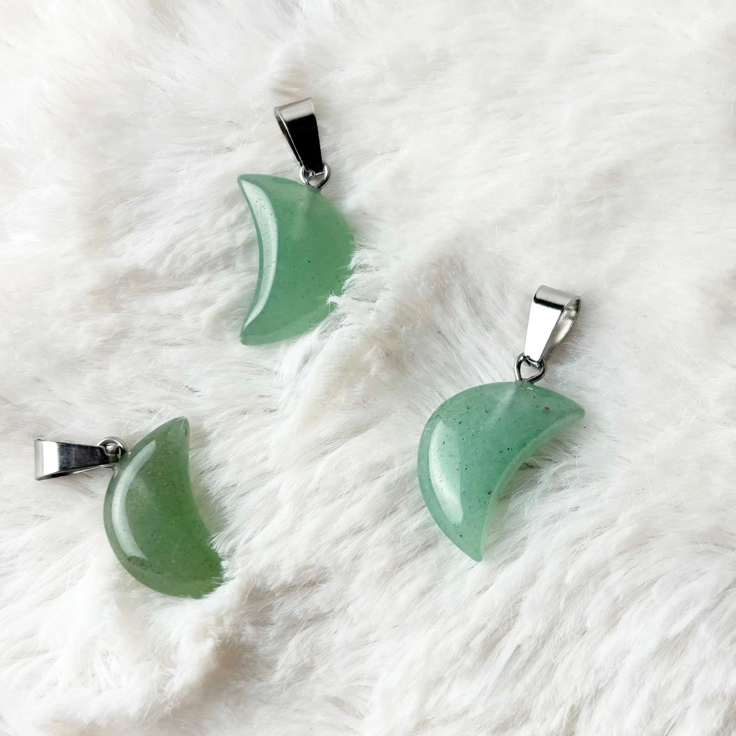 Four green moon-shaped pendants on a white fur surface