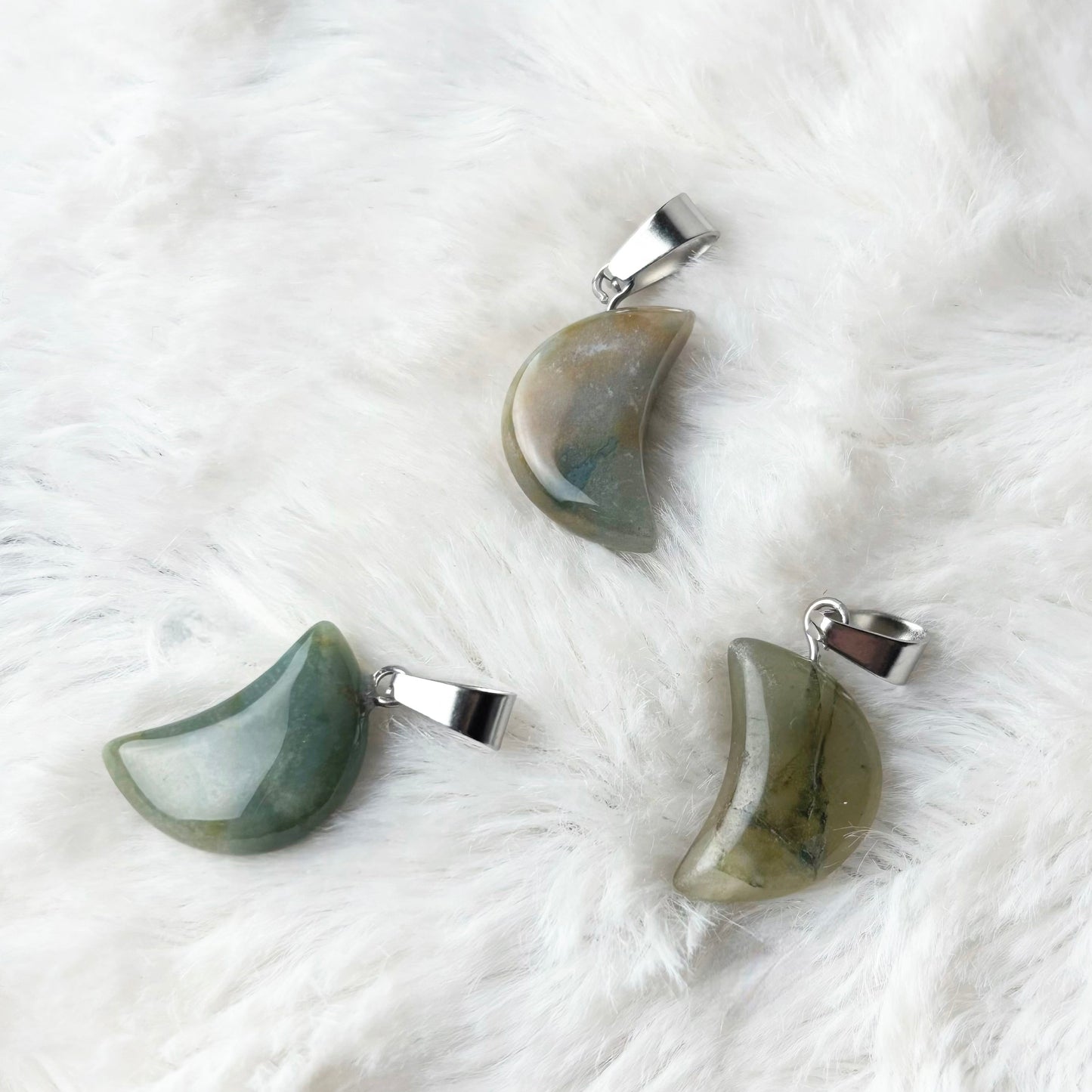 Three green stone pendants on a white fur surface