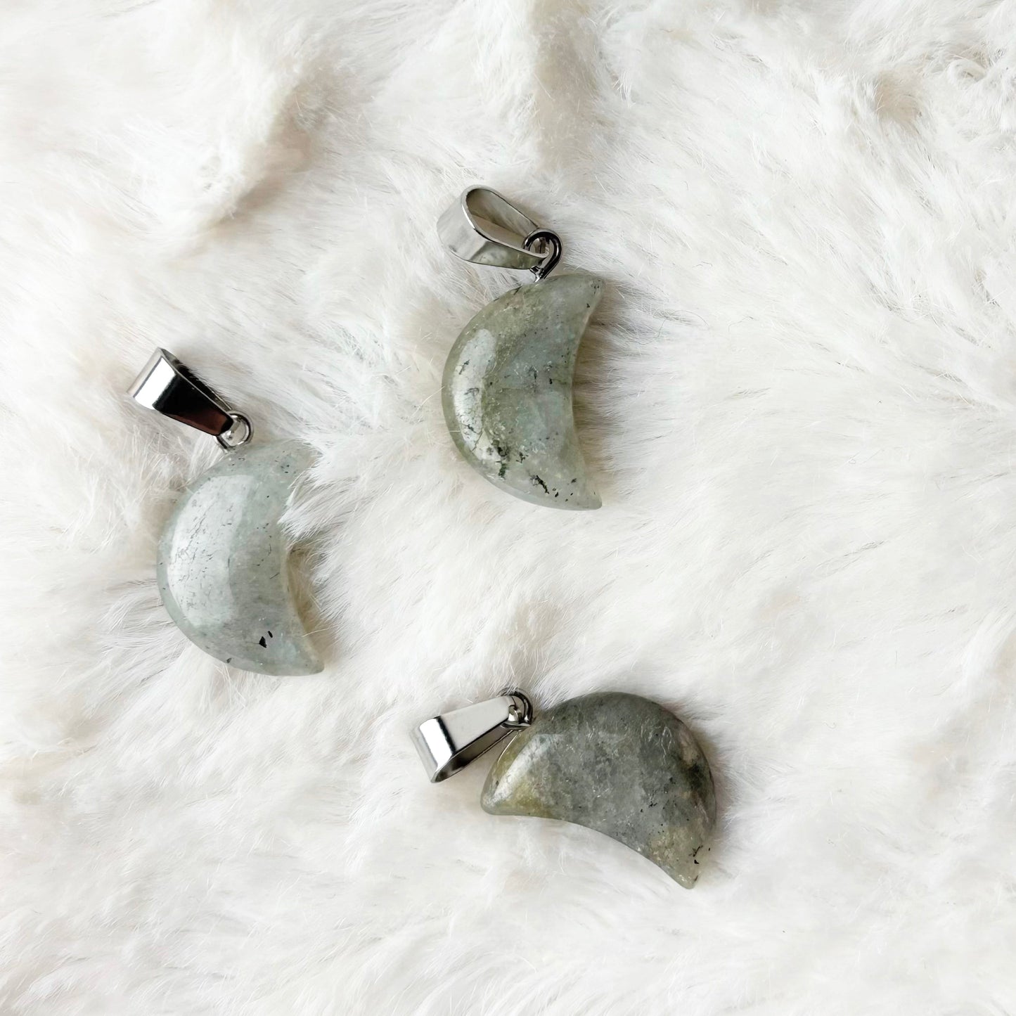 Four stone pendants shaped like moons on a white textured surface
