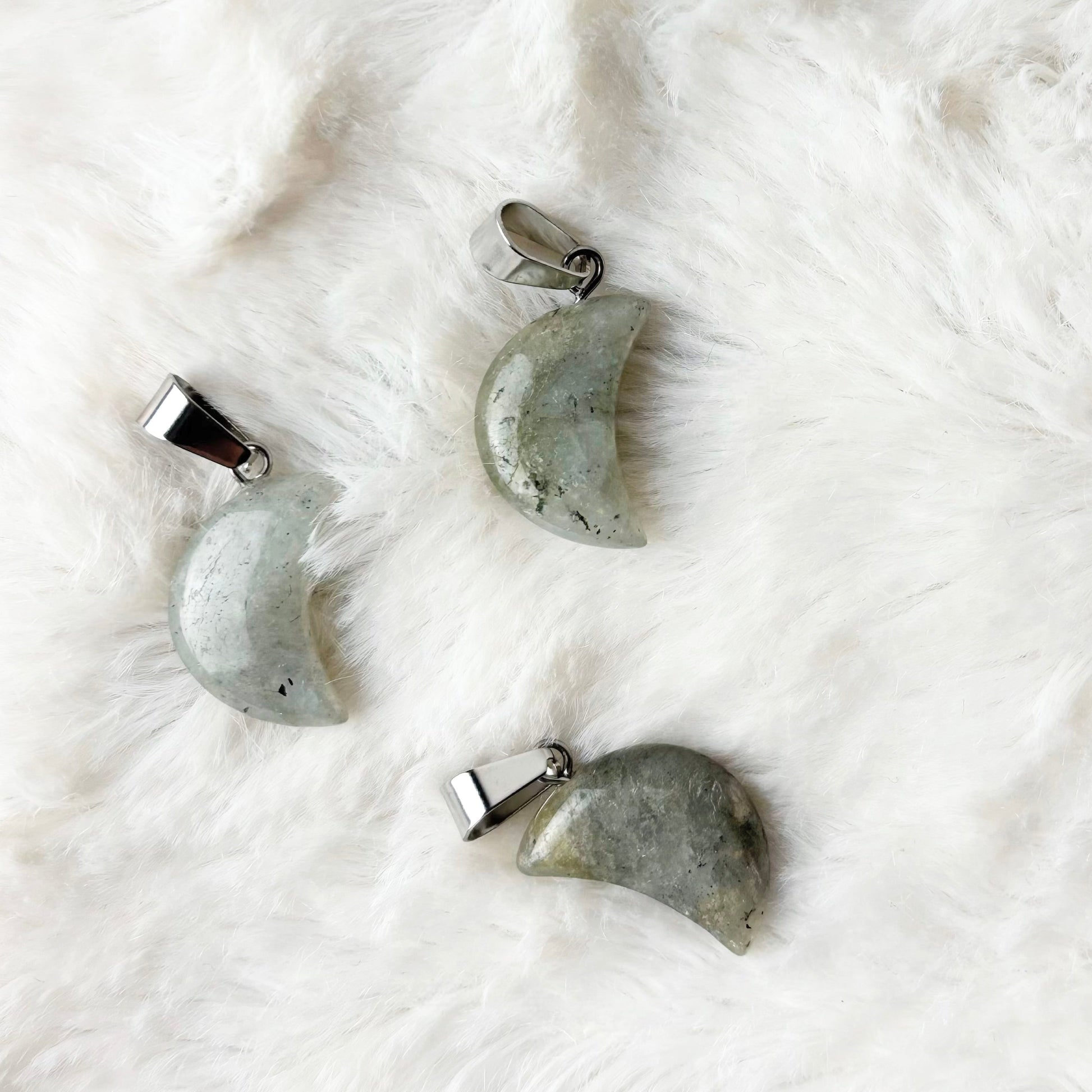 Four stone pendants shaped like moons on a white textured surface