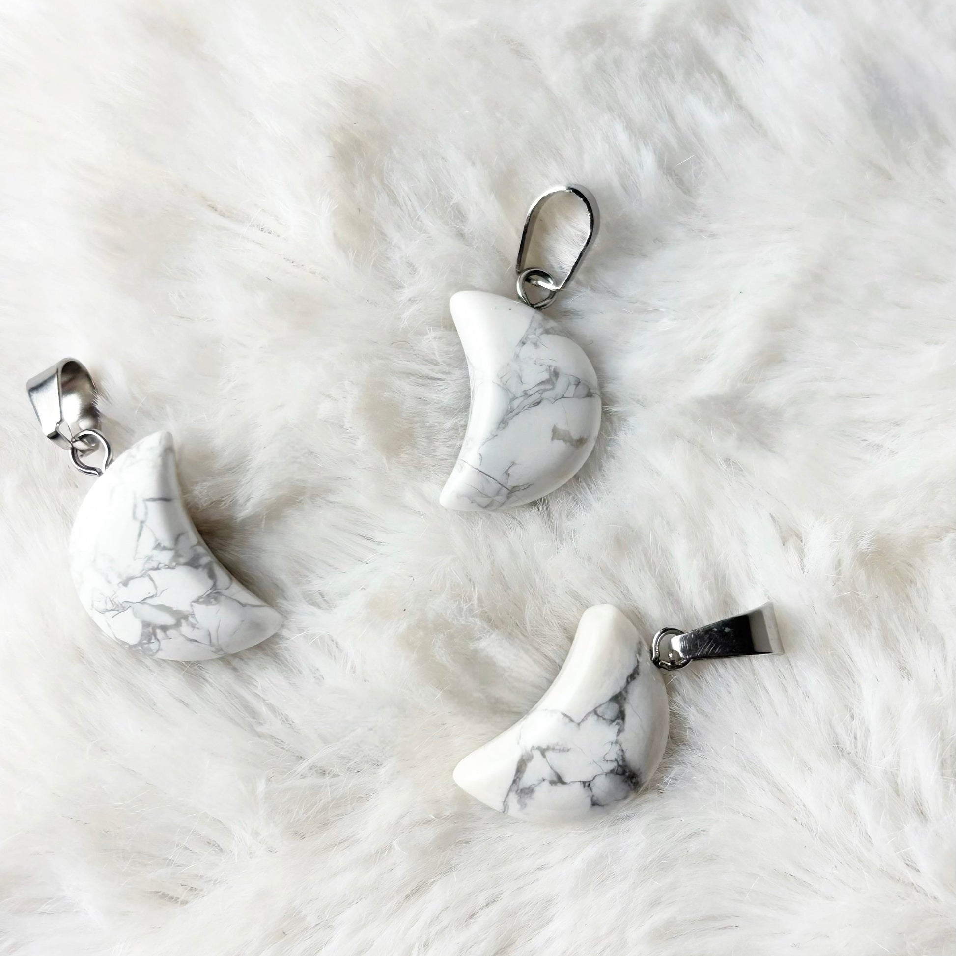 Three marble-textured crescent moon pendants on a white fur surface