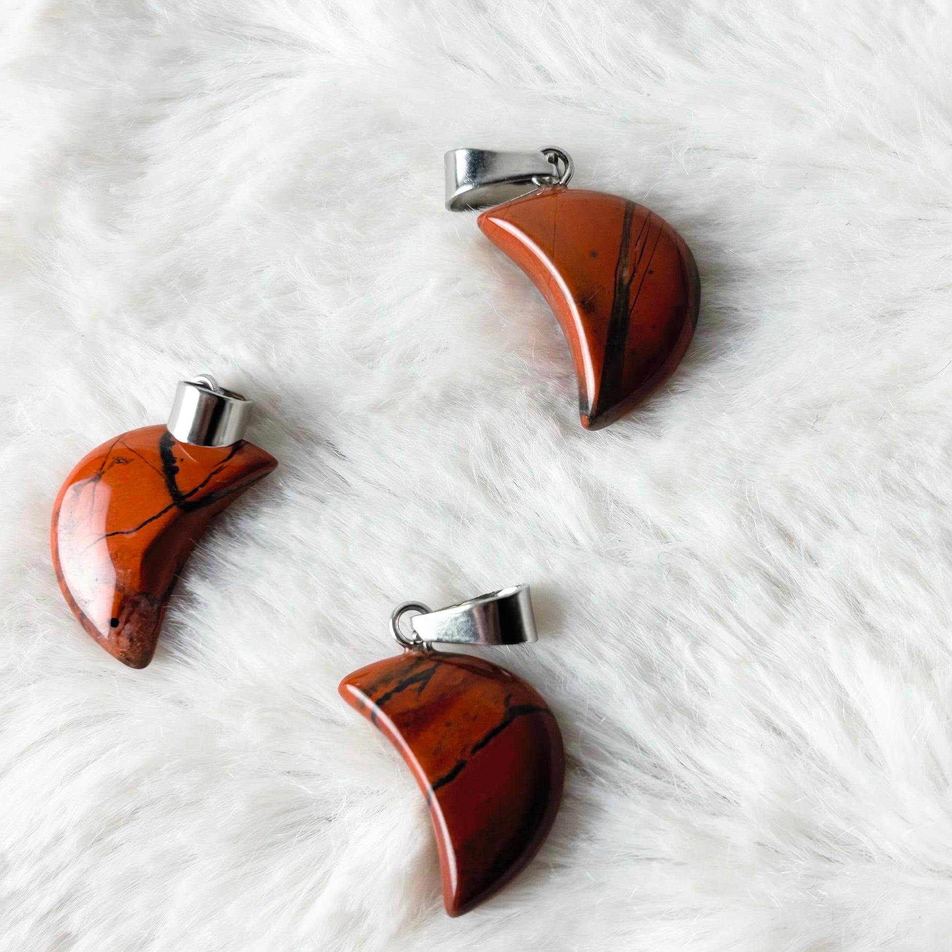 Three brown stone pendants with silver clasps on a white textured surface