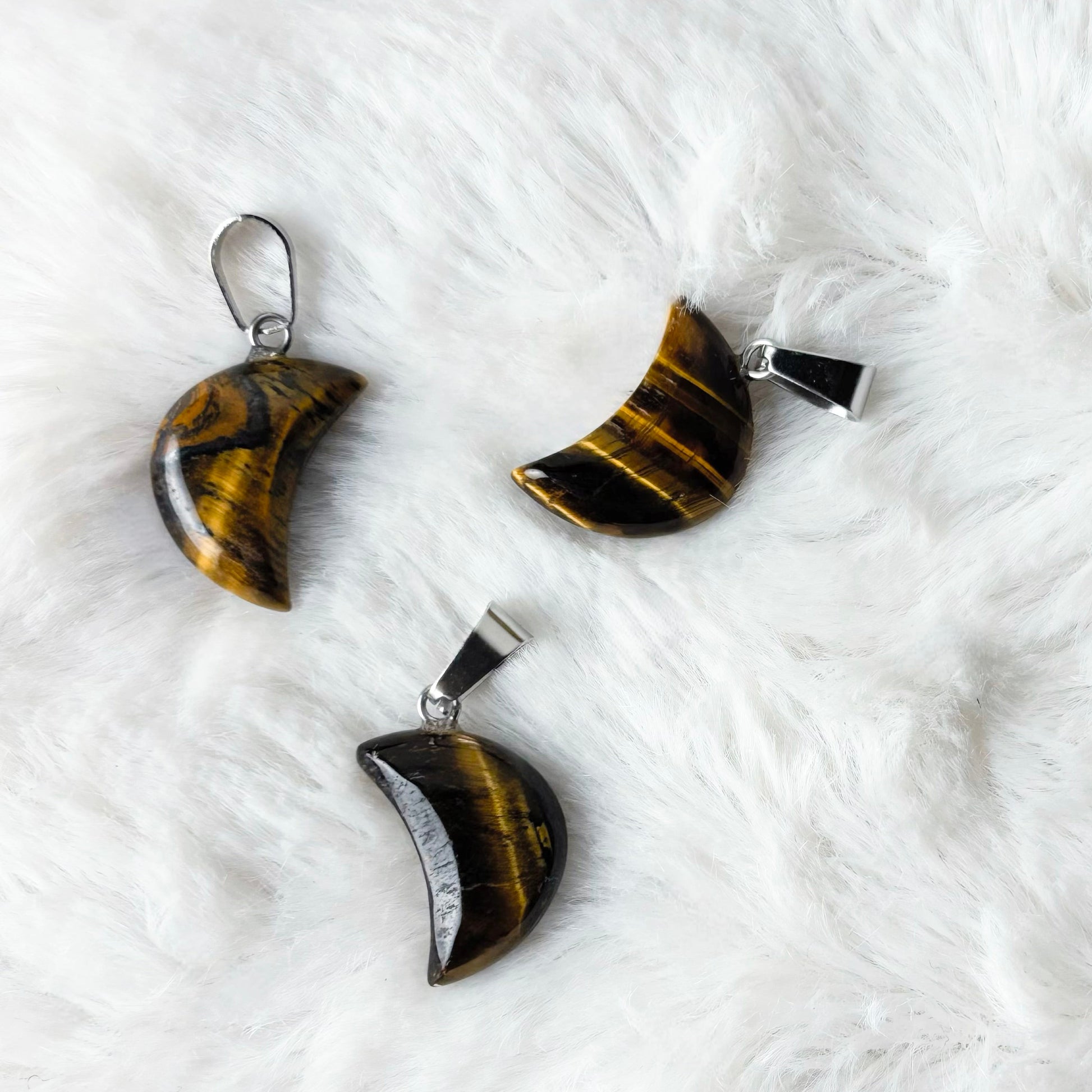 Three tiger eye pendants on a white fur surface