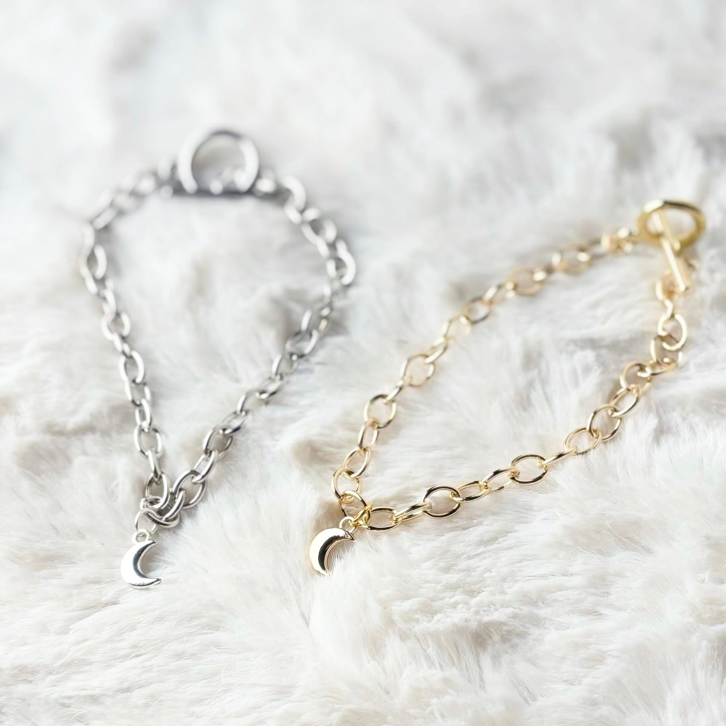 Two bracelets, one silver and one gold, on a white fluffy surface.