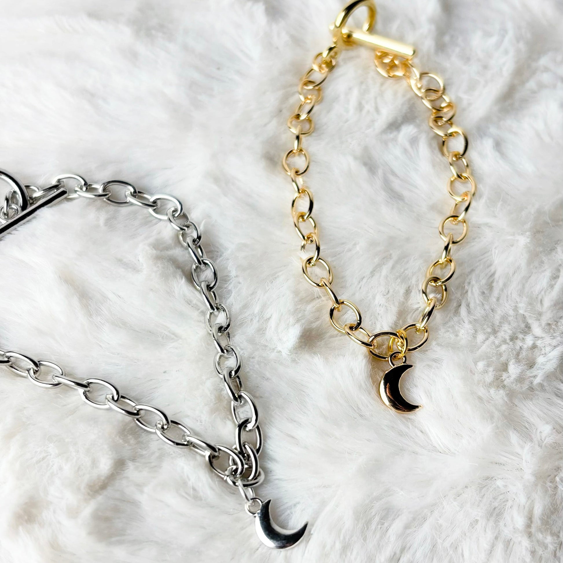 Two chain bracelets, one gold and one silver, on a white fluffy surface.