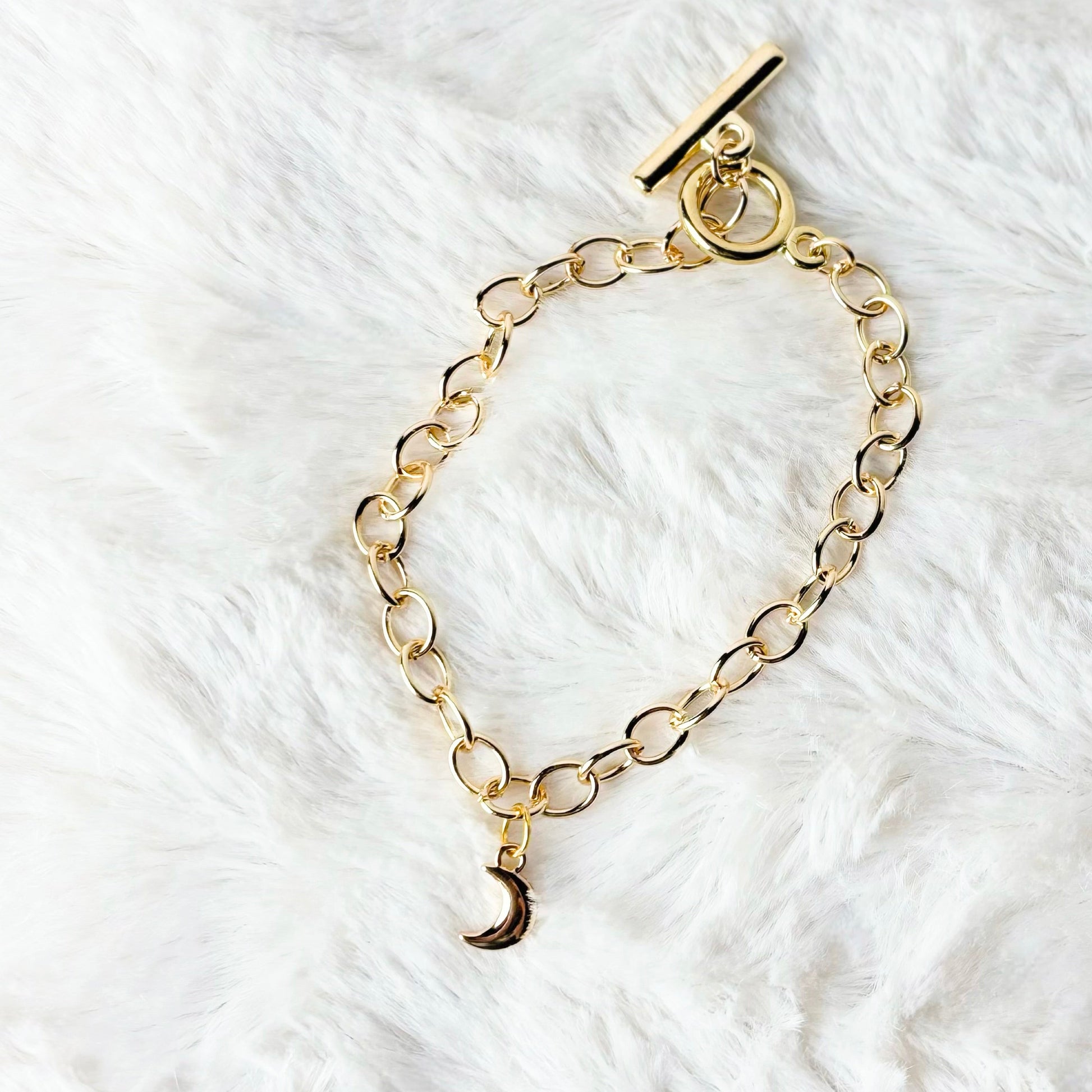 Gold chain bracelet with a moon charm on a white fur background