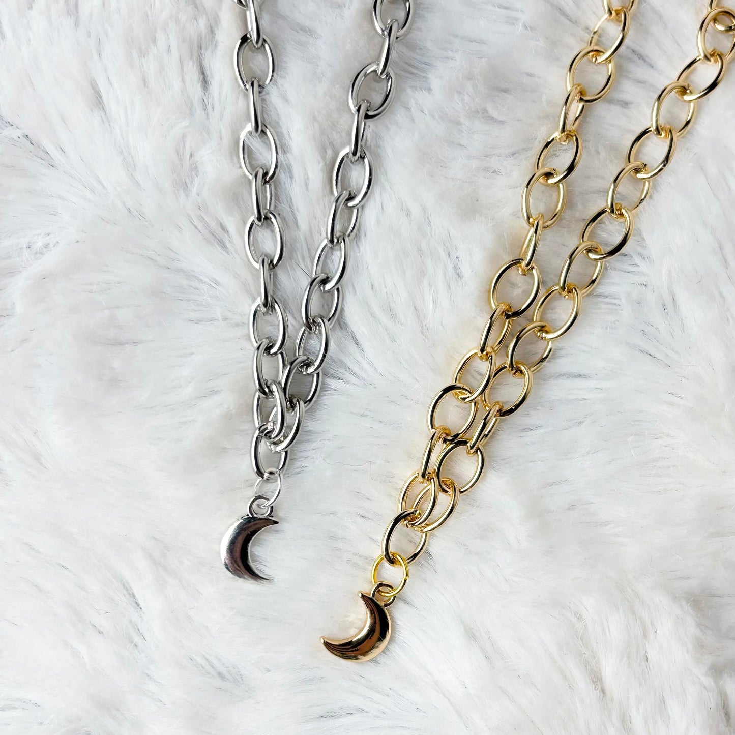 Two chain necklaces with crescent moon pendants on a white fur background